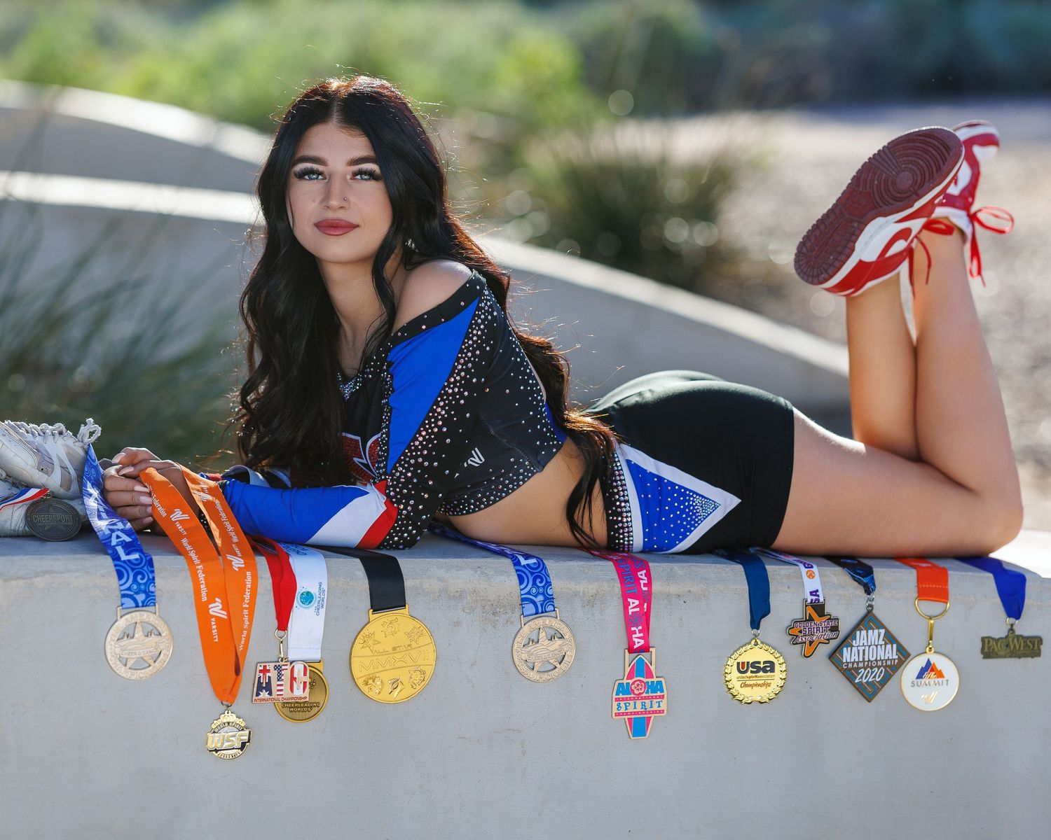 Young female athlete poses with numerous medals in a cheerleading uniform showcasing her championship achievements.
