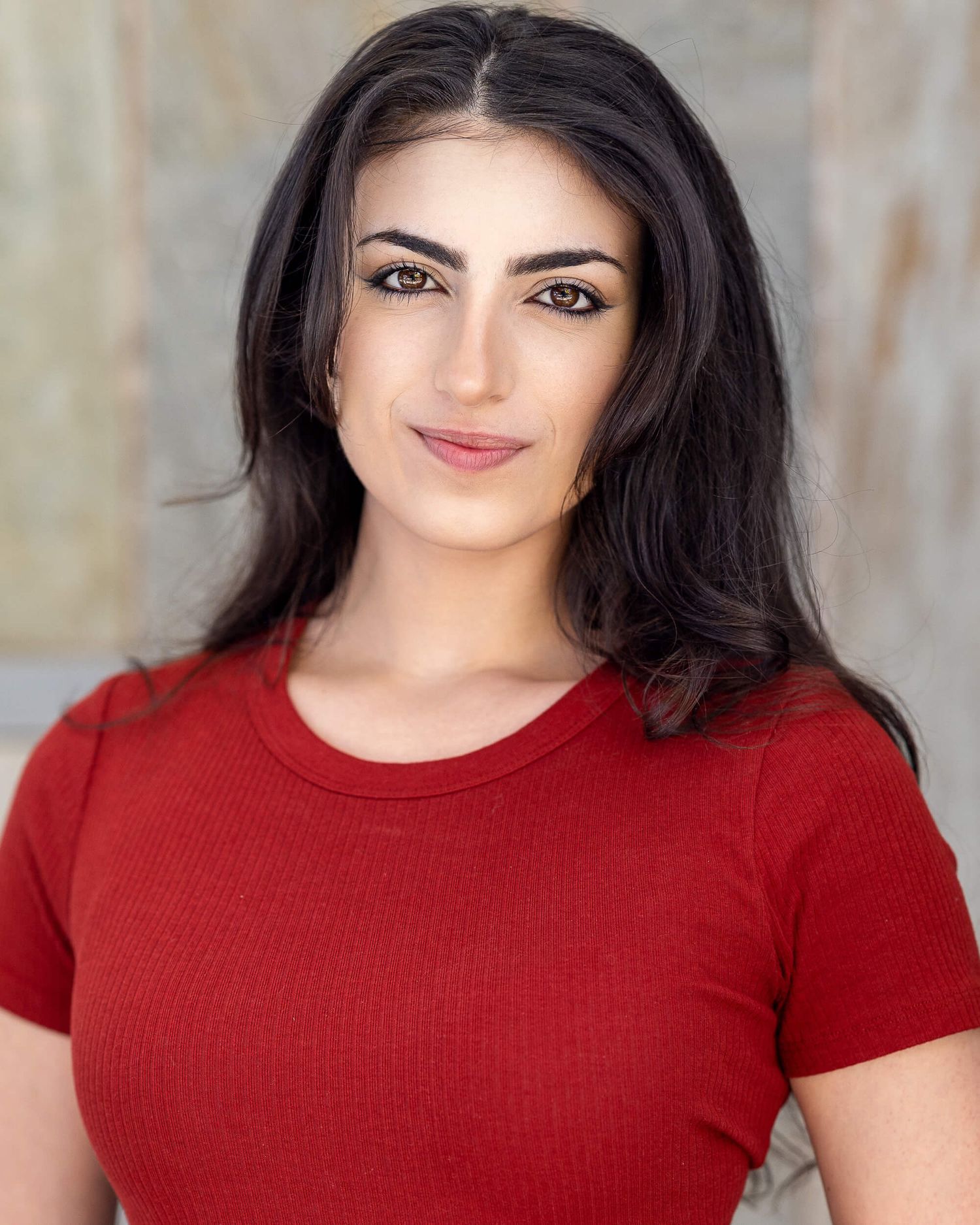 Young woman with long dark hair wearing a red ribbed t-shirt poses for a professional headshot.