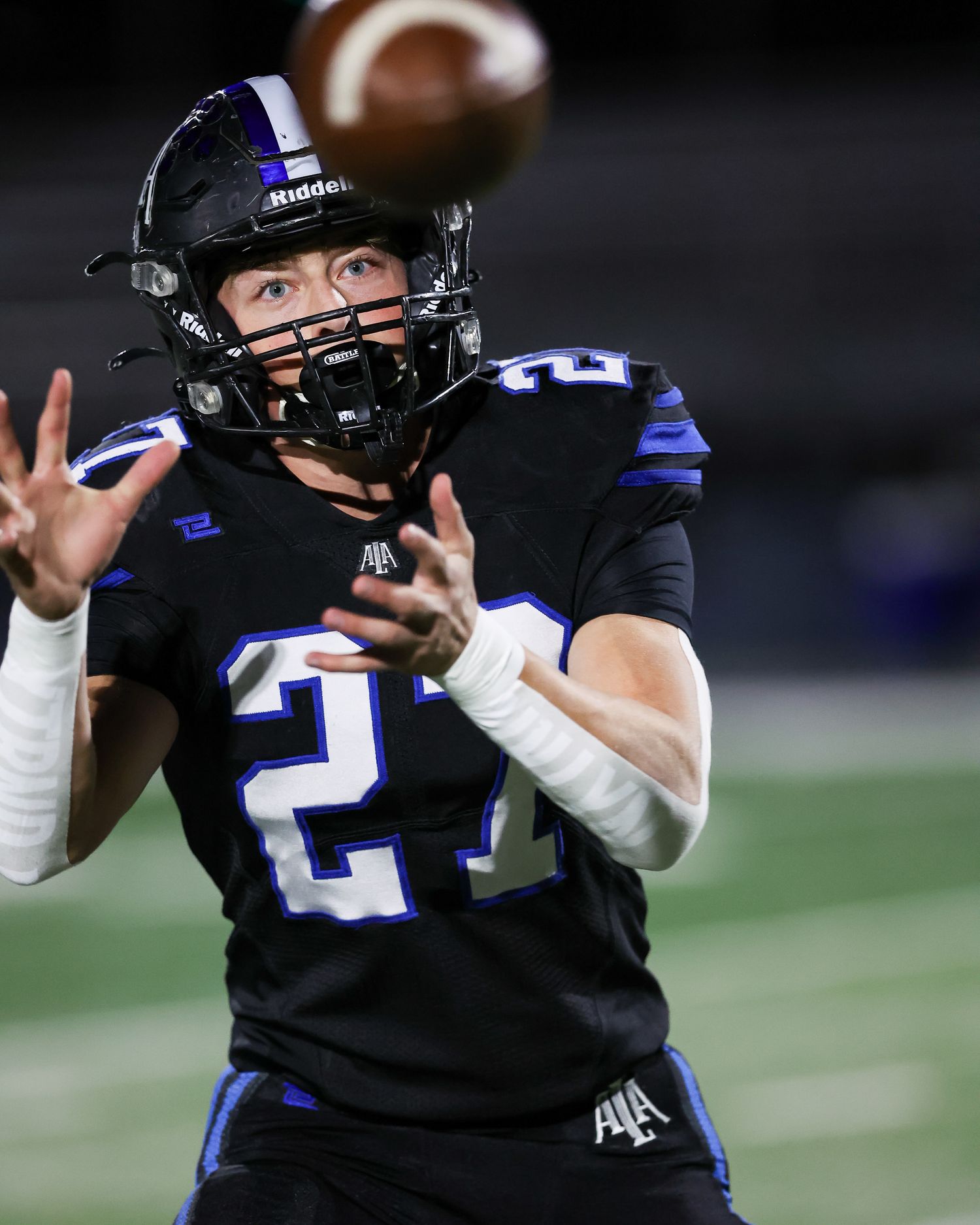 Football player in black and blue uniform number 27 catching a pass under stadium lights.