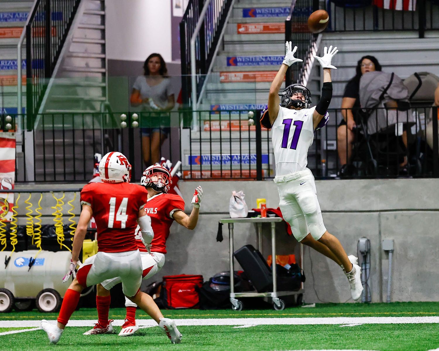 Football player #11 in purple leaps to catch a pass during an indoor game.