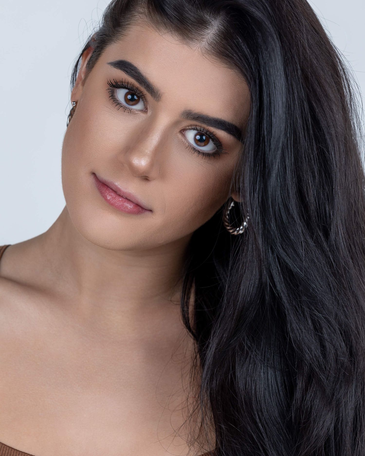 Young woman with long black hair and hoop earrings poses with a serious expression.