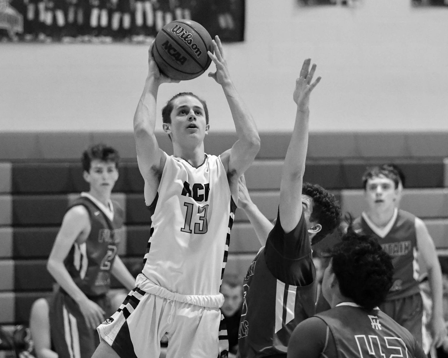 High school basketball player number 13 shoots over a defender during an indoor game.