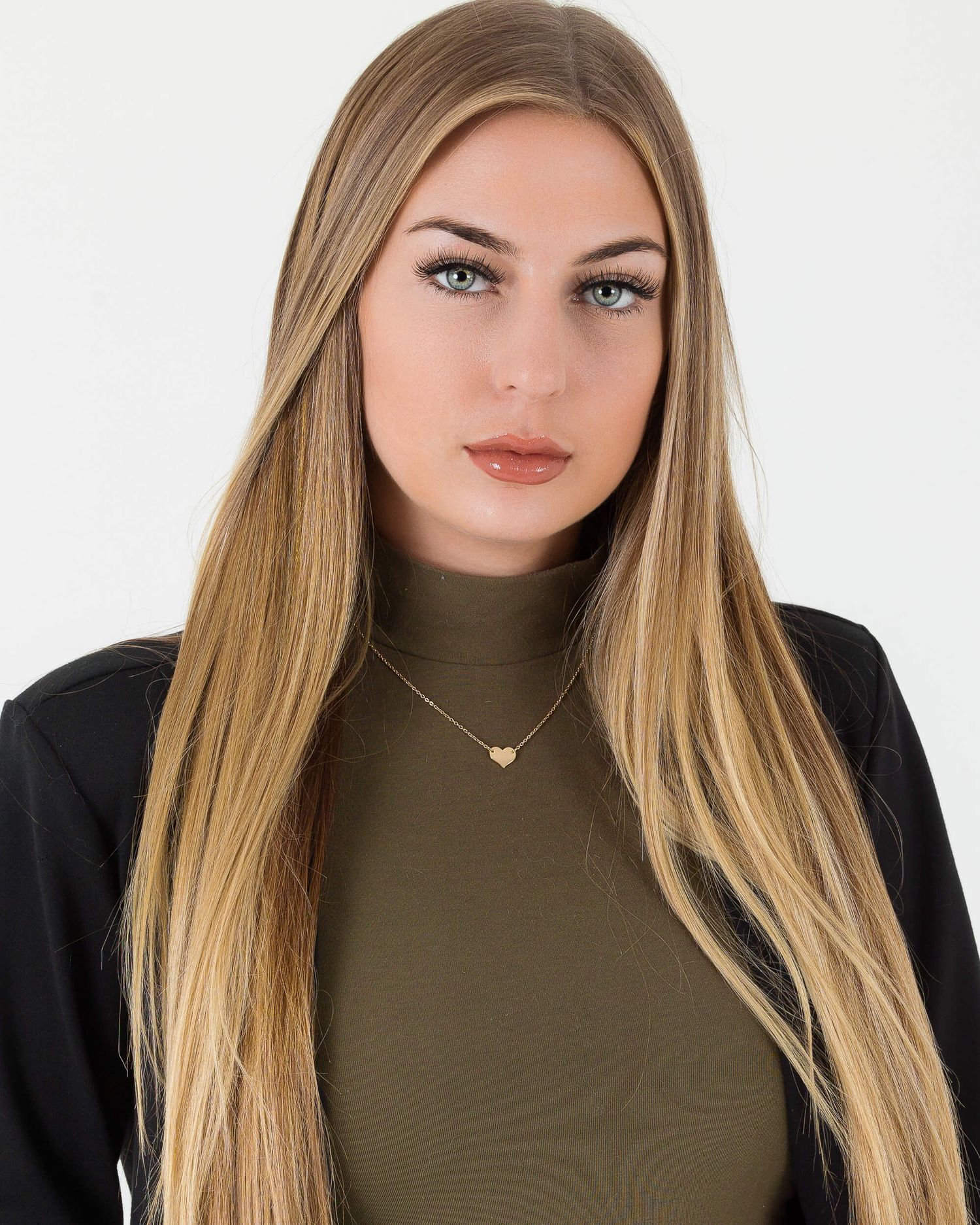Young woman with long blonde hair wearing an olive turtleneck and gold necklace against a white background.