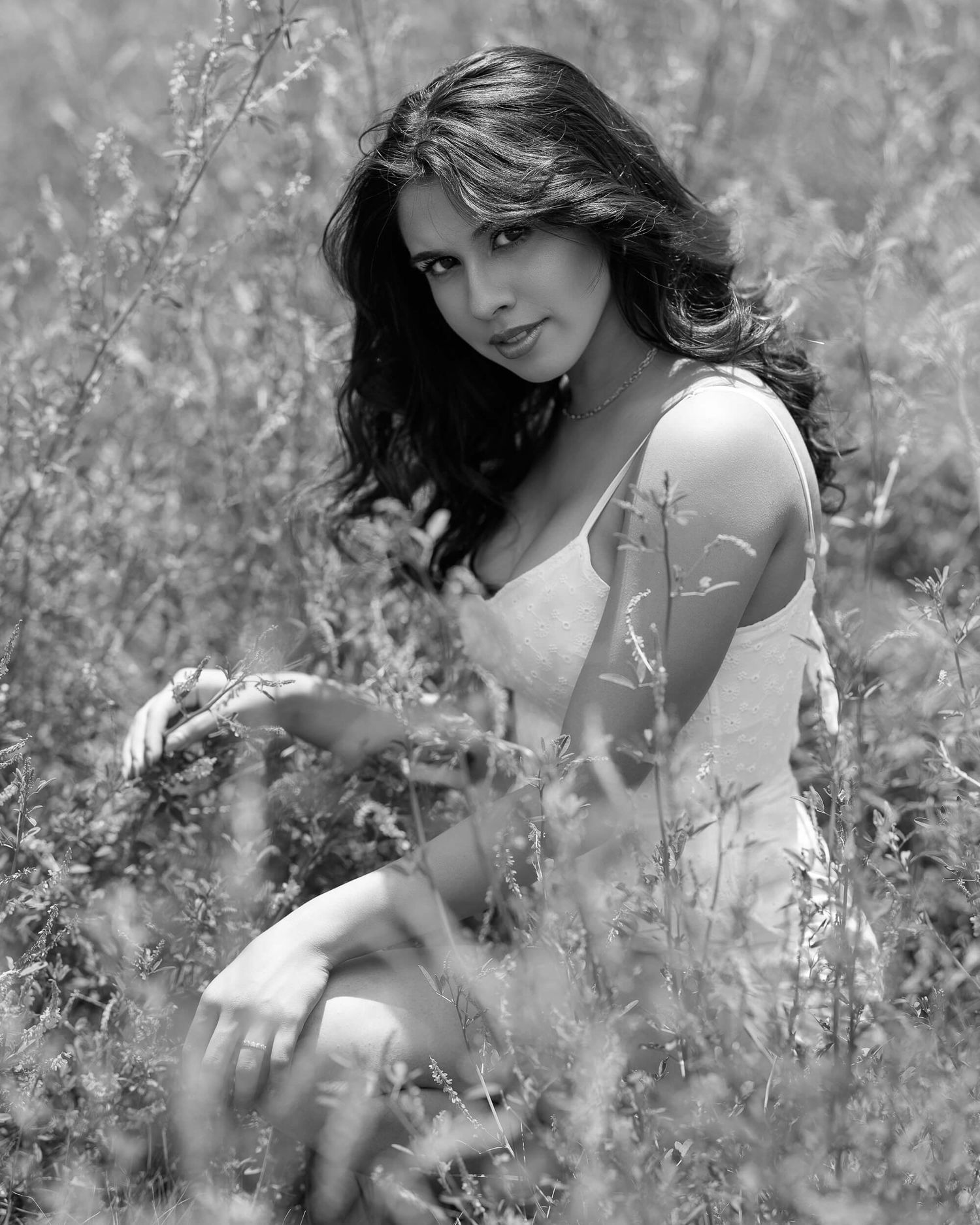 Black and white portrait of a brunette woman sitting in a wildflower field.