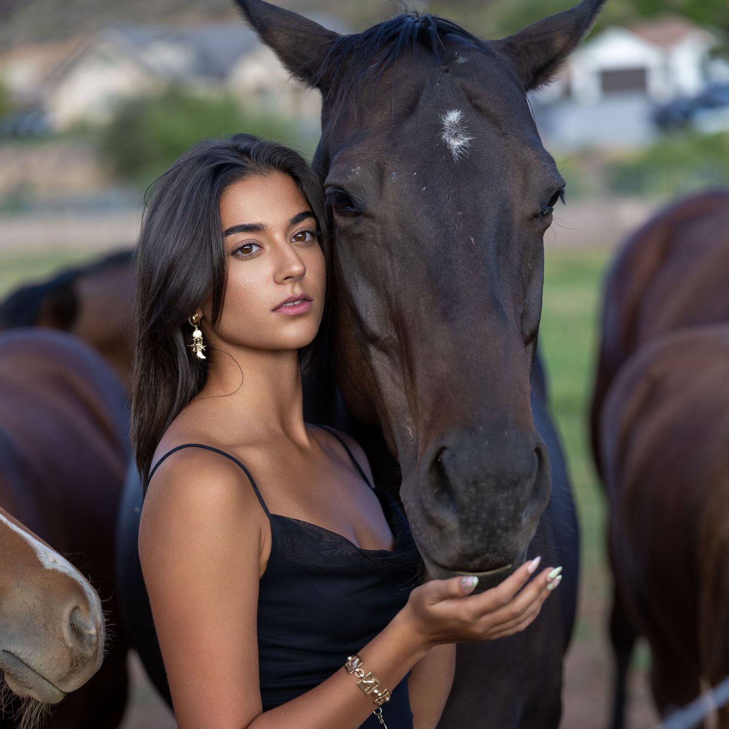 Young woman with dark hair posing beside a dark horse on a ranch.