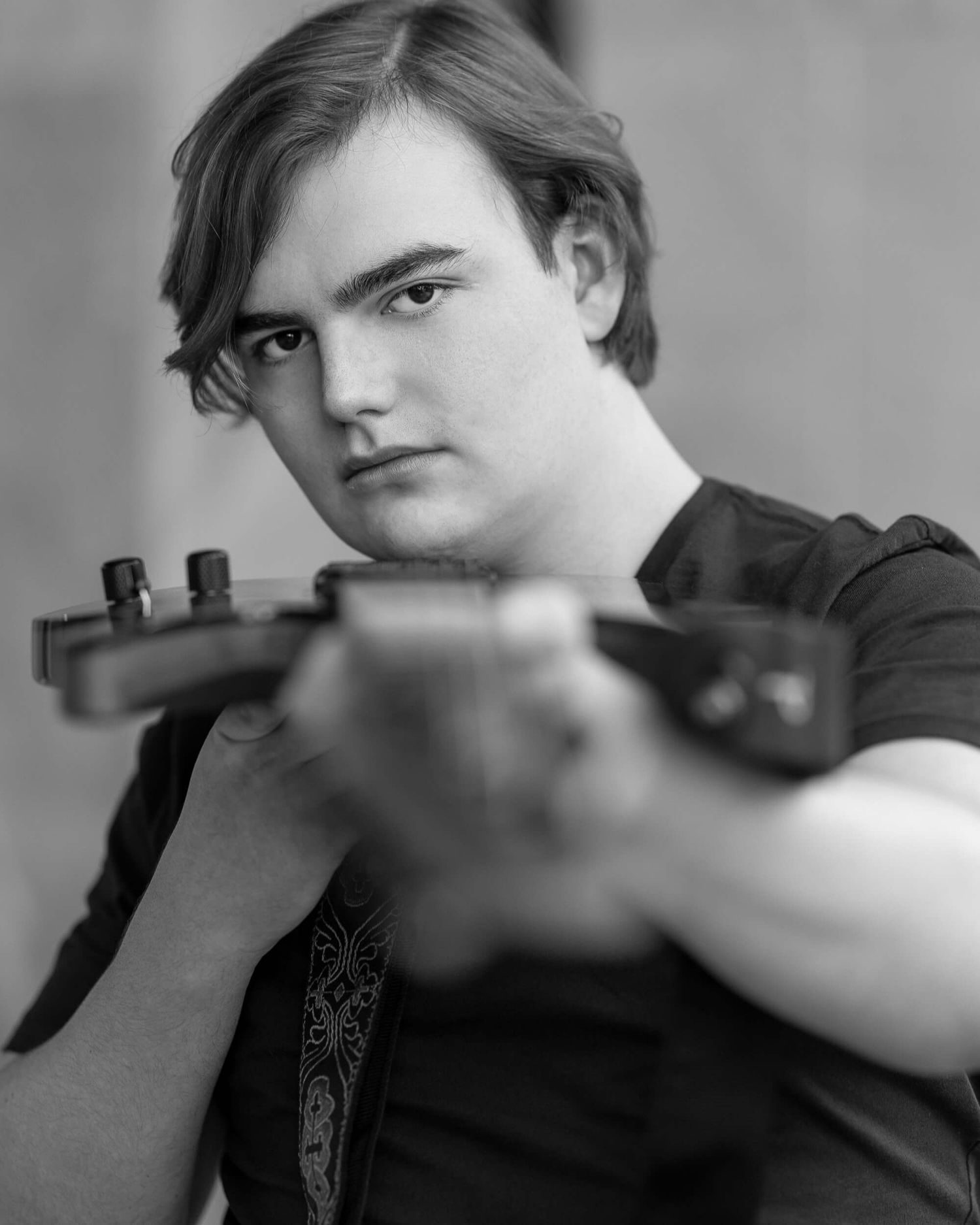 Black and white portrait of a young man holding a guitar neck toward the camera with a serious expression.