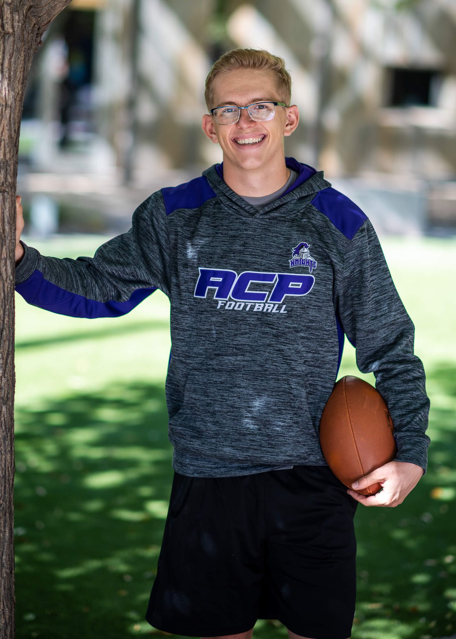 Smiling teen in ACP Football hoodie holding football outdoors.