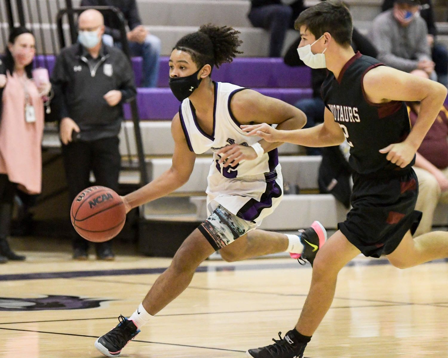 Two high school basketball players compete as one dribbles past a defender wearing masks.