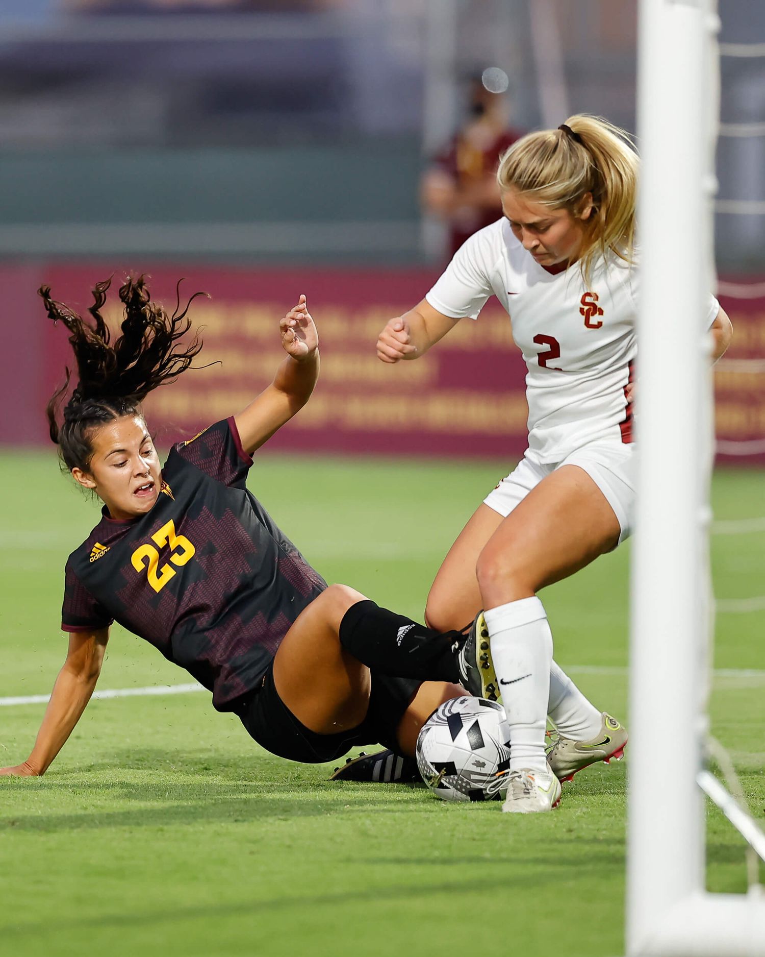 Two female soccer players competing for the ball near the goal during a USC vs ASU college soccer match.