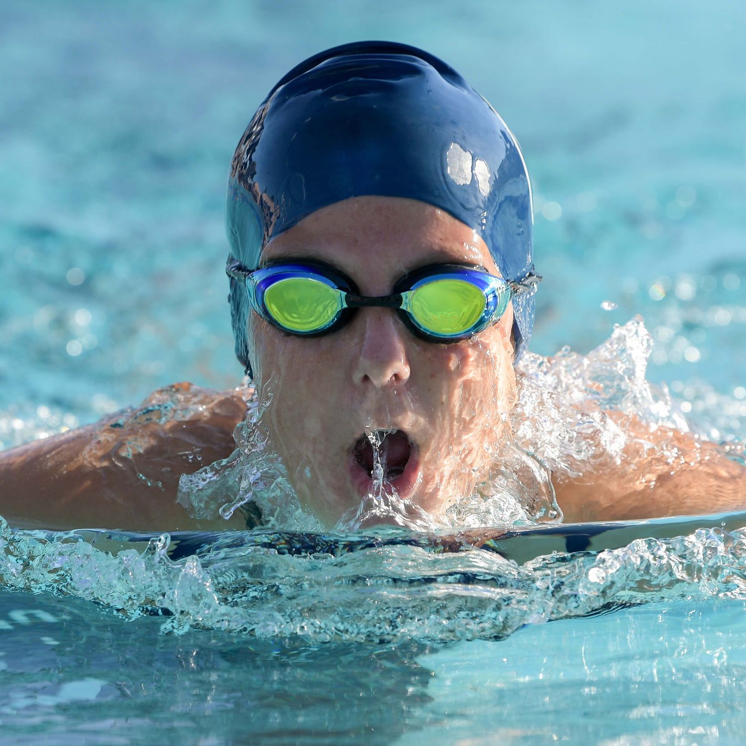 Male competitive swimmer wearing goggles and swim cap surfaces during a breaststroke race.