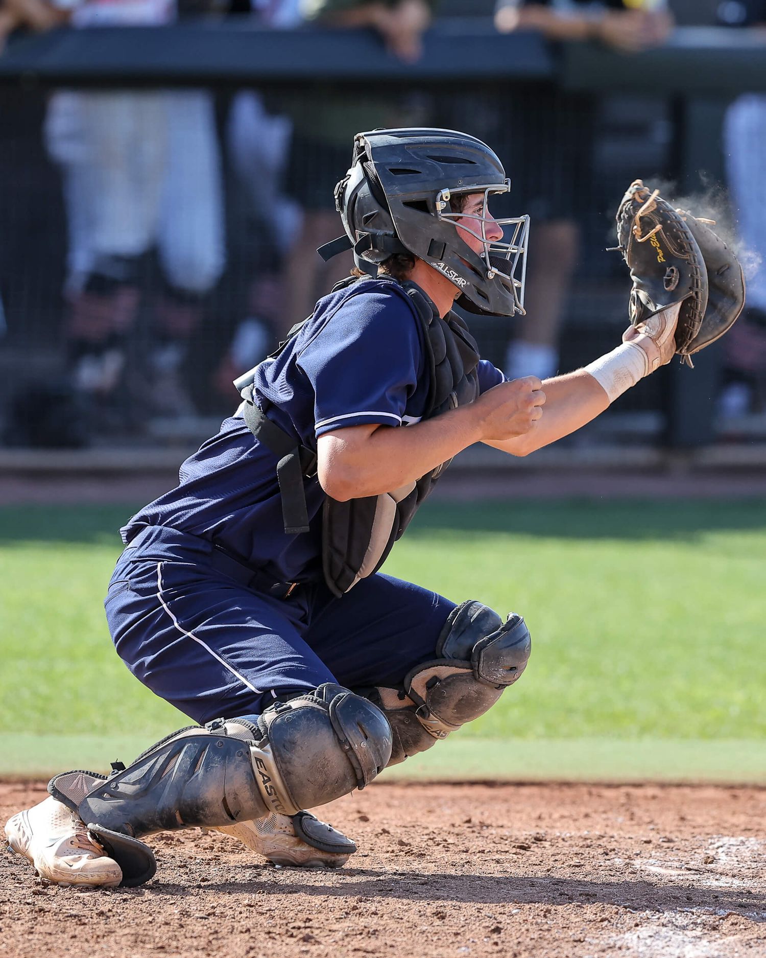 Baseball catcher in navy uniform crouches to receive a pitch during a game.