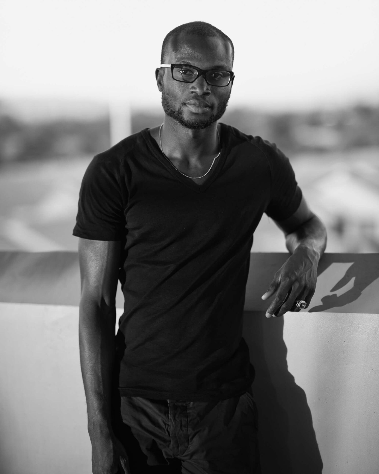 Black and white portrait of man in black t-shirt leaning on wall.