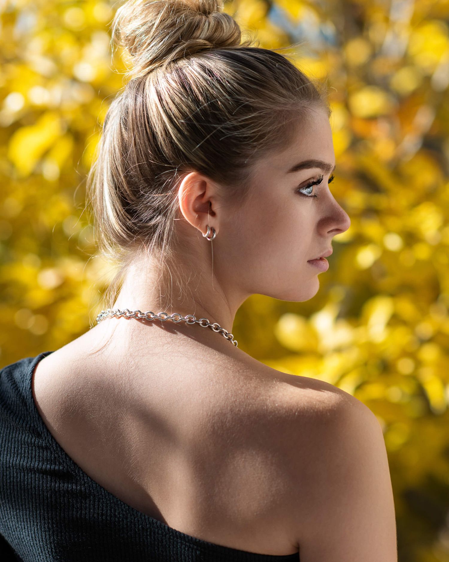 Side profile of blonde woman with updo hairstyle wearing choker necklace outdoors.