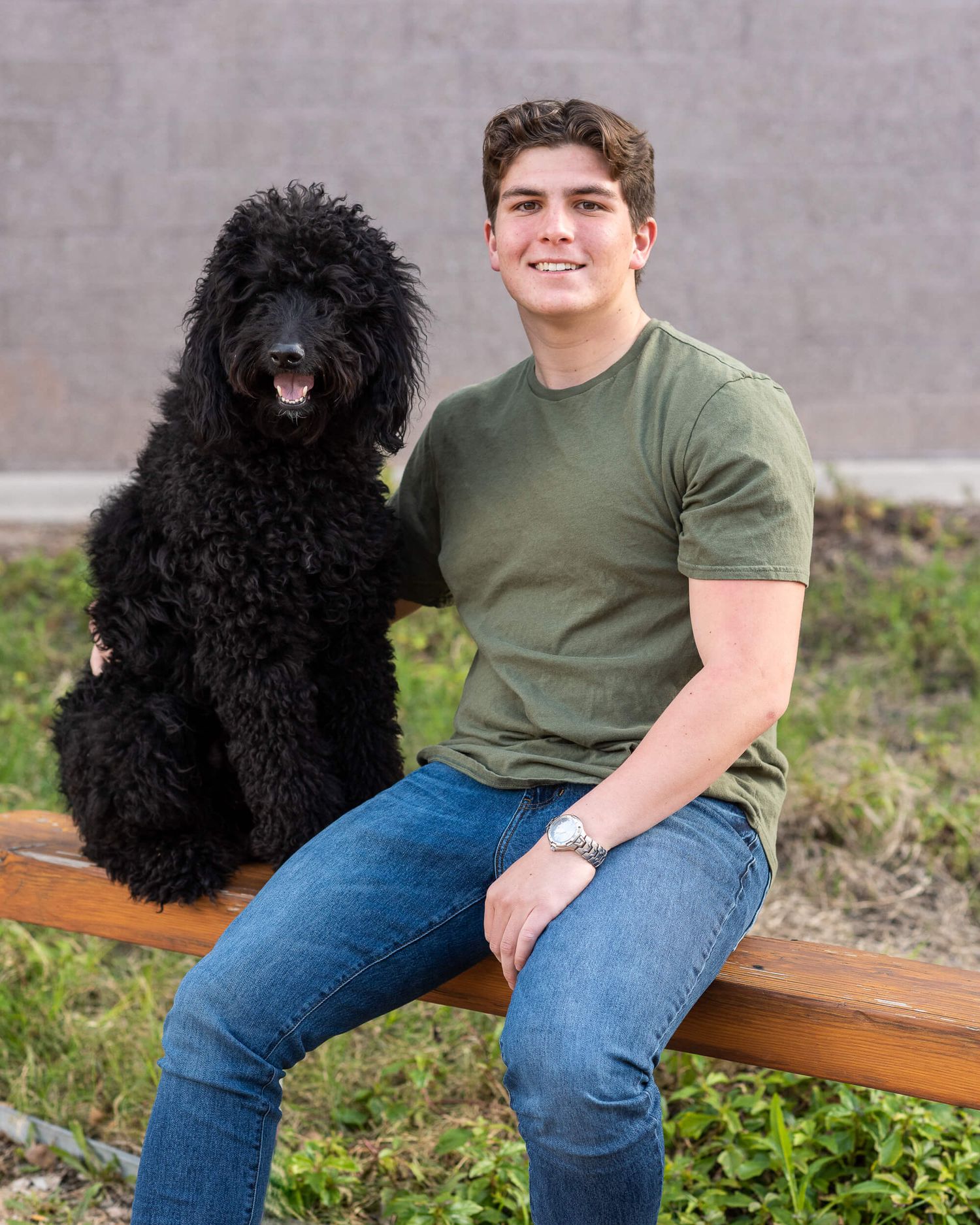 Young man sitting on bench with black standard poodle dog outdoors.
