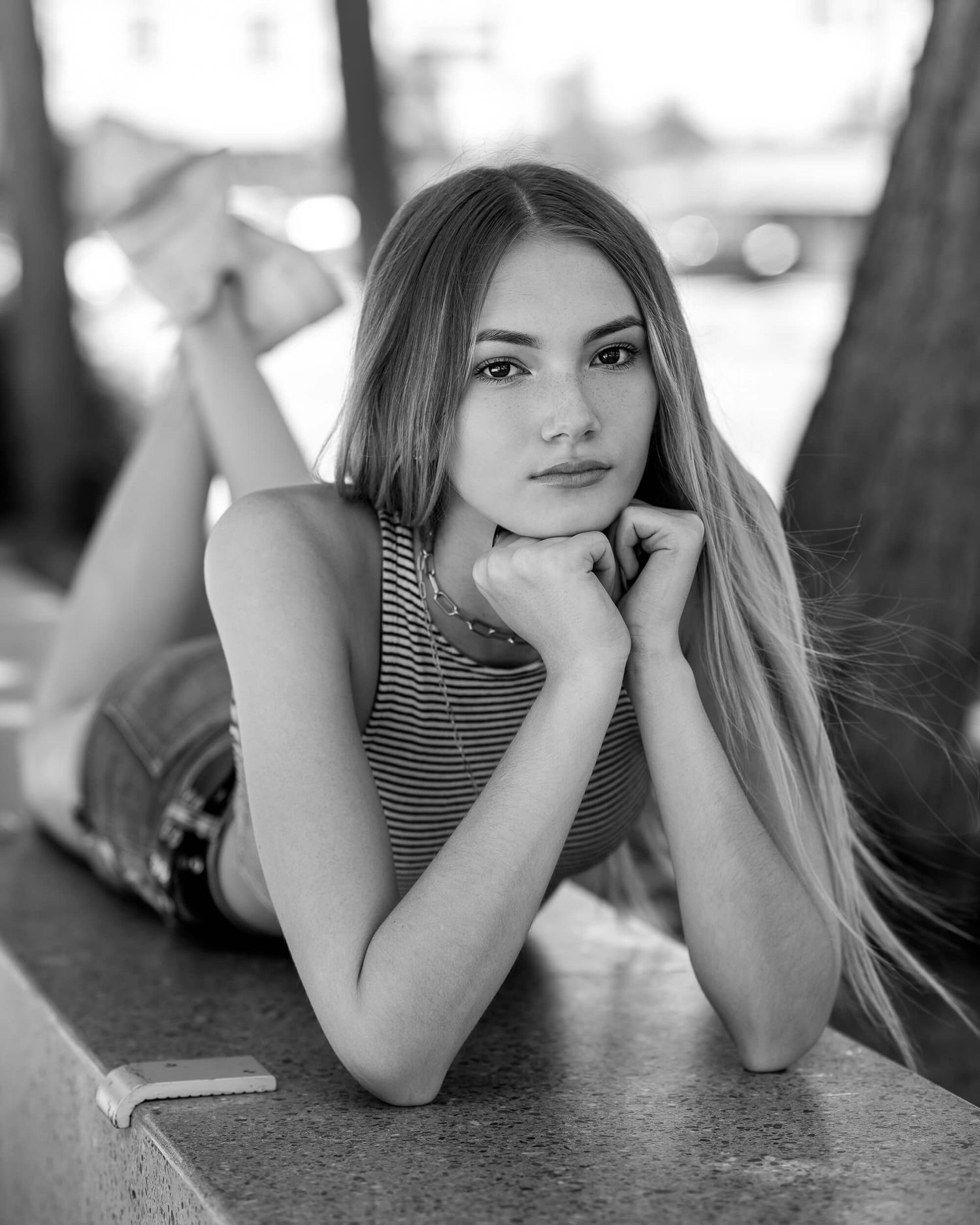 Young woman with long blonde hair poses on a ledge in a striped top and denim shorts in a black and white portrait.