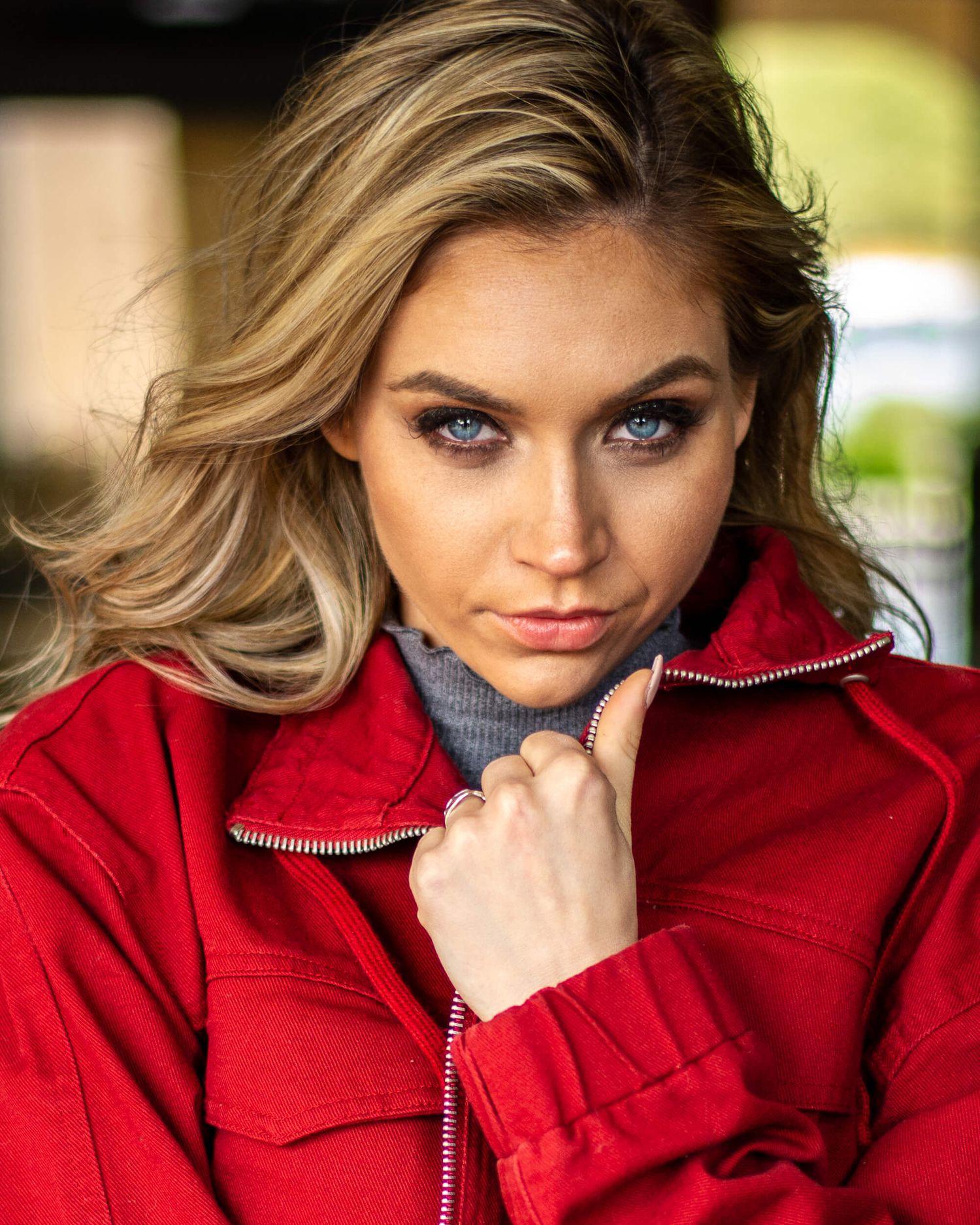 Blonde woman with blue eyes wearing red jacket posing outdoors.