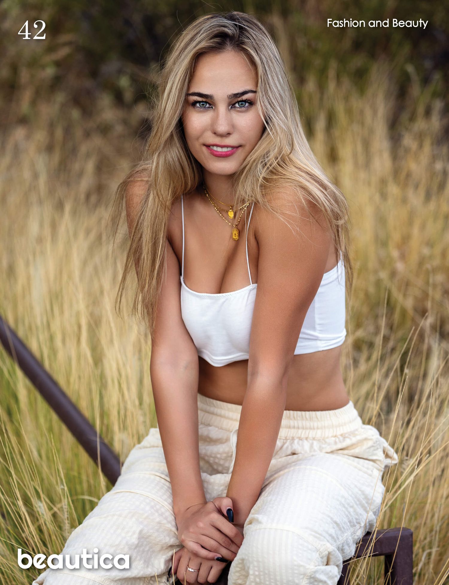 Blonde woman with blue eyes in white bralette and pants sits outdoors for Beautica magazine shoot.