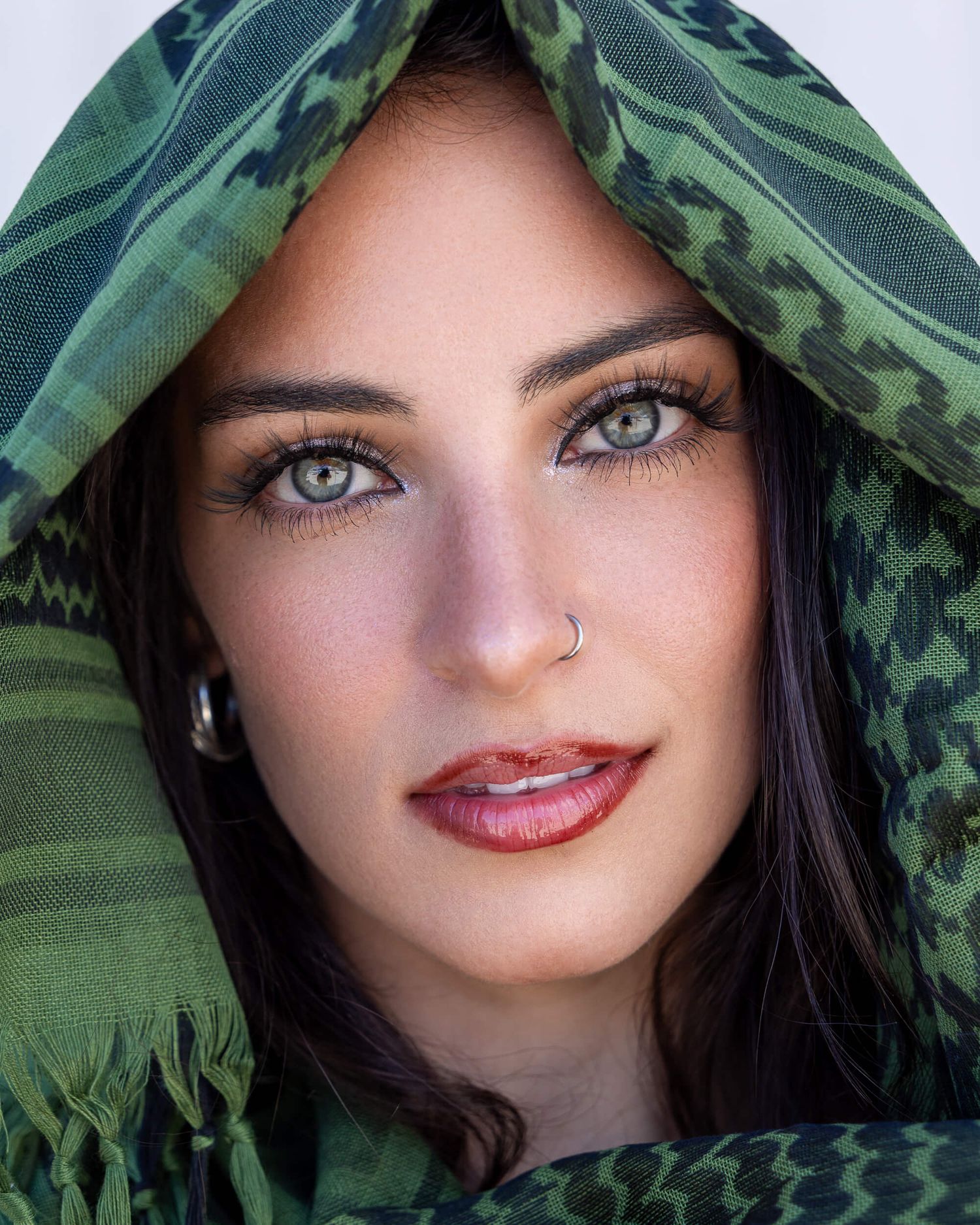 Close-up portrait of woman with striking green eyes wearing a green patterned headscarf and nose ring.