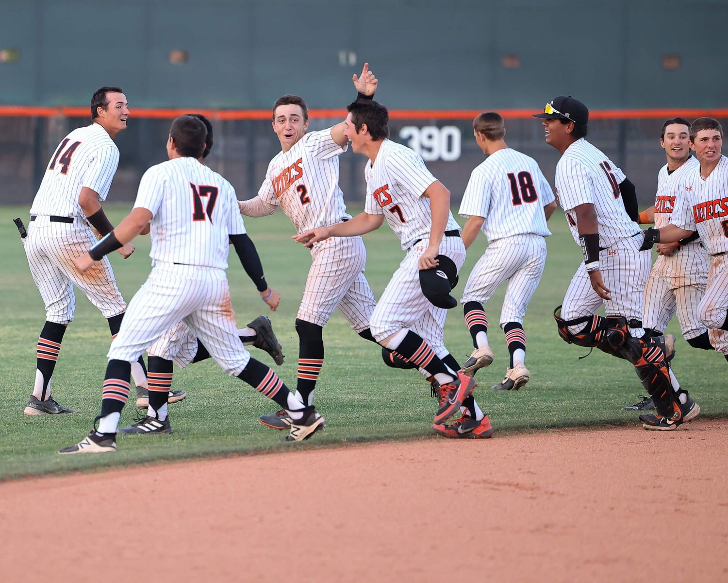 Baseball team celebrates victory on field as players in white pinstripe uniforms rush together after winning game.