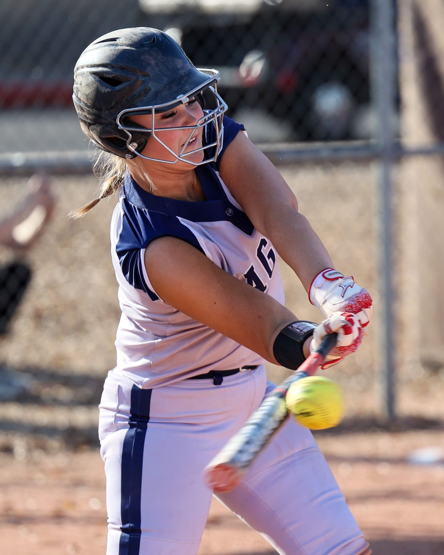 Female softball batter makes contact with yellow ball during outdoor game.