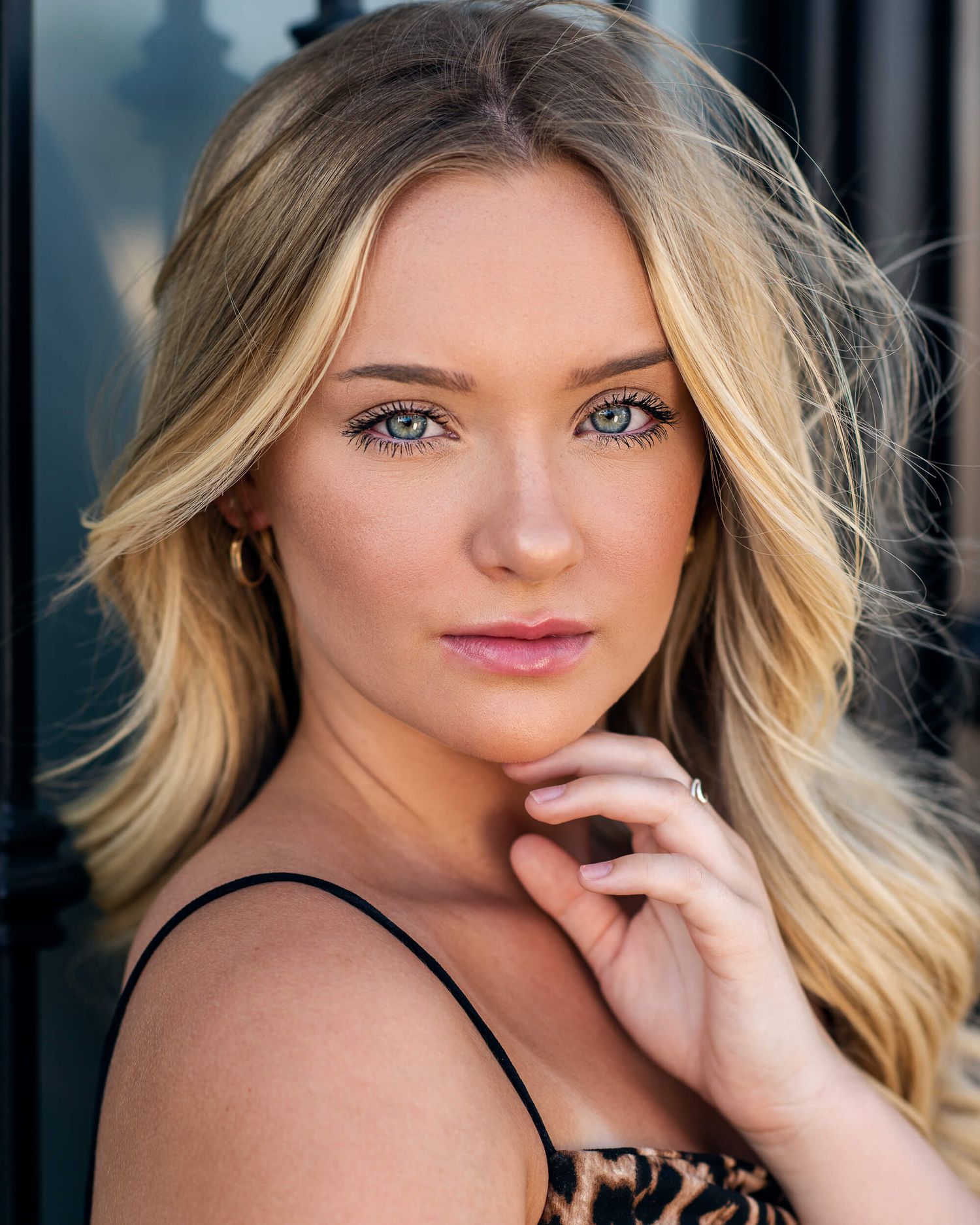 Blonde woman with blue eyes and wavy hair wearing leopard print top in outdoor portrait.