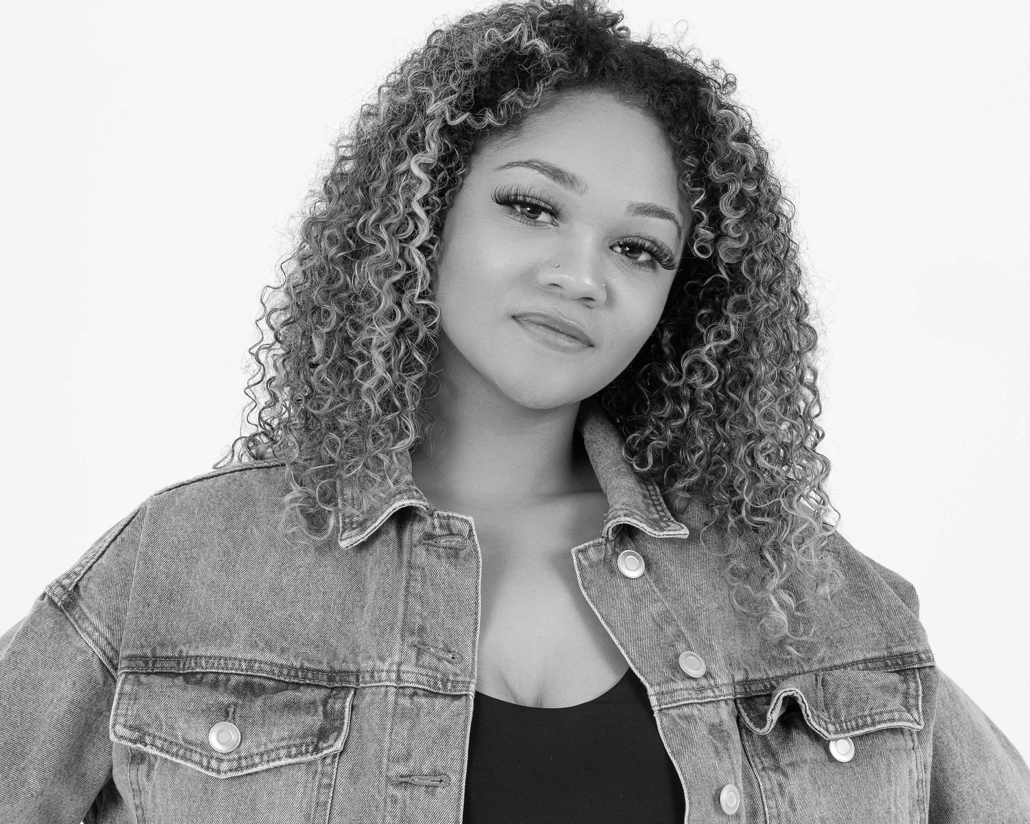 Black and white portrait of a young woman with curly hair wearing a denim jacket.