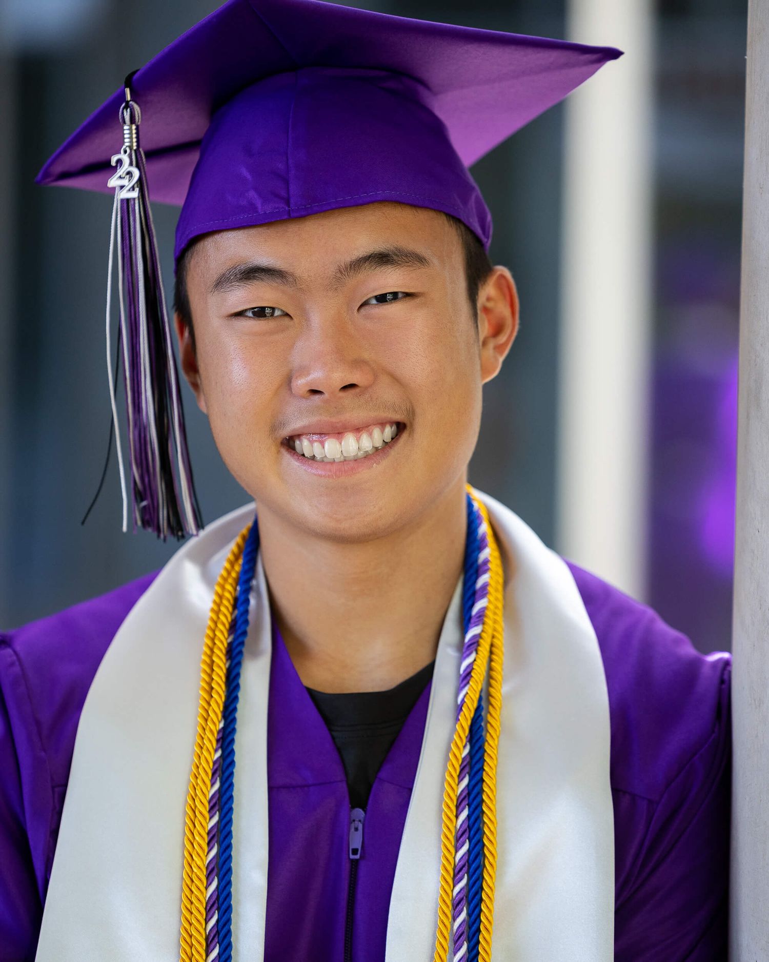 Smiling graduate in purple cap and gown with honor cords at graduation ceremony.