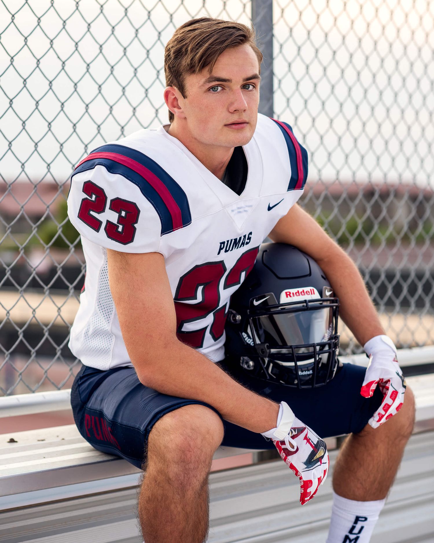 Young football player wearing number 23 Pumas jersey sitting on bleachers holding a Riddell helmet.
