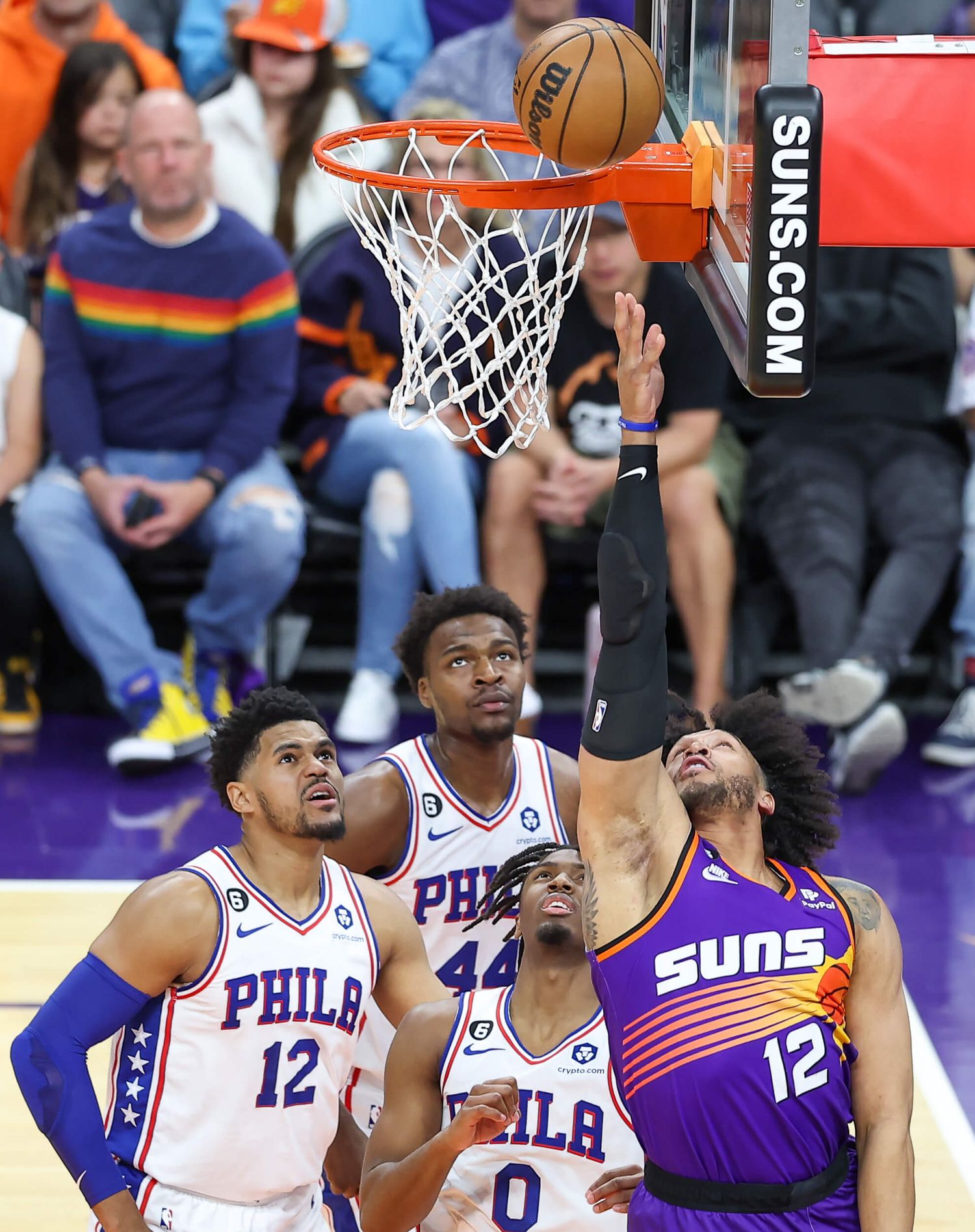 Phoenix Suns player drives to basket against Philadelphia 76ers defenders in NBA game.