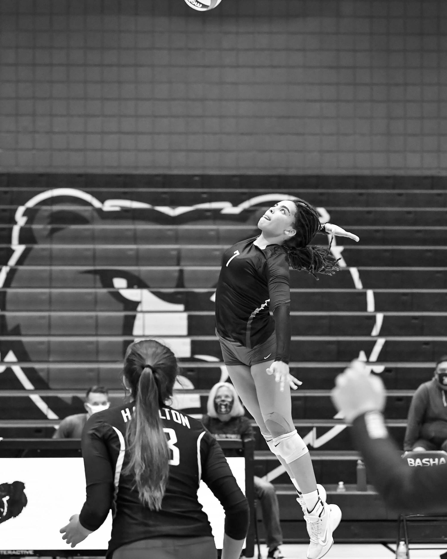 Female volleyball player jumps to spike the ball during an indoor high school match in black and white.