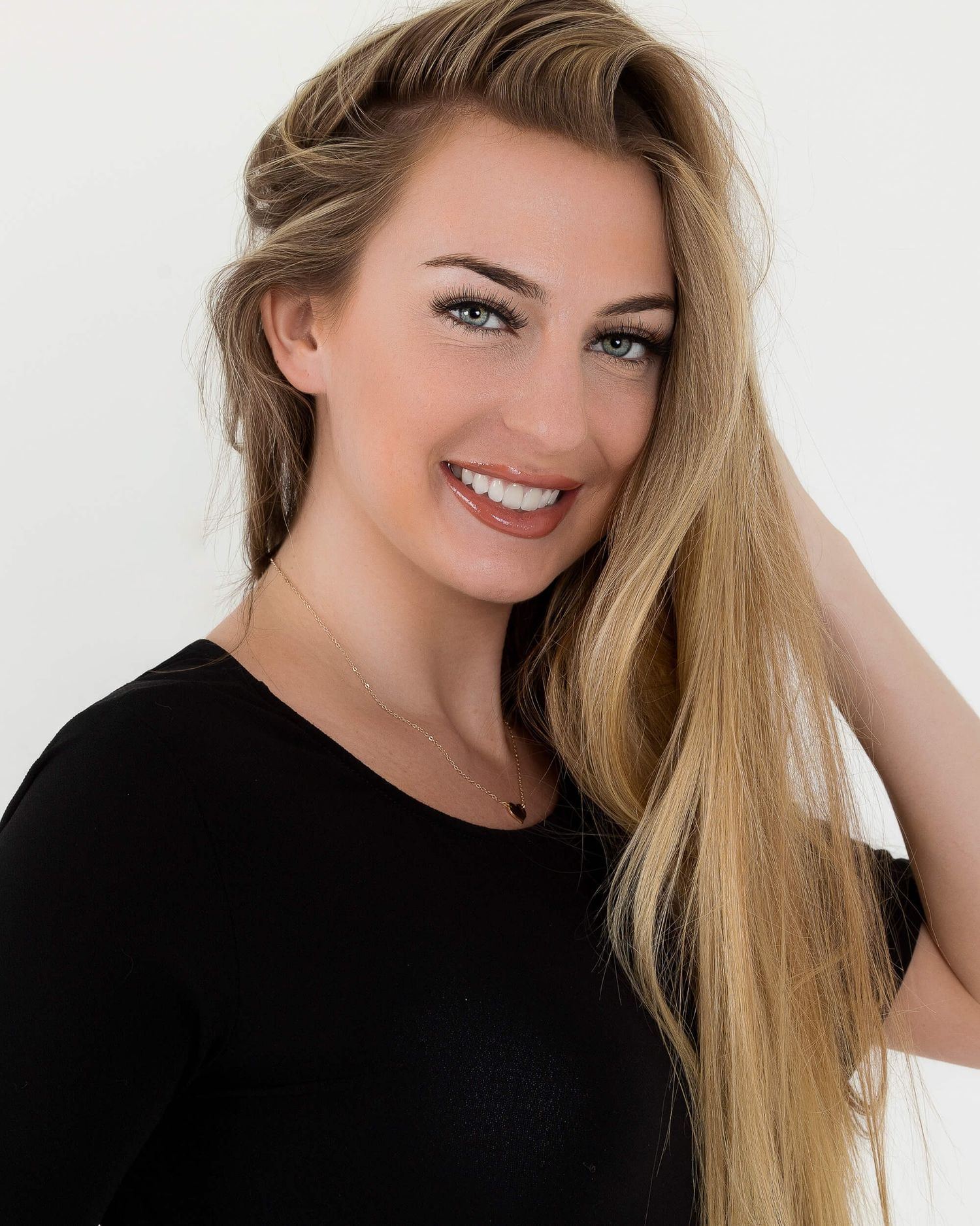 Smiling blonde woman with long straight hair wearing a black top against a white background.