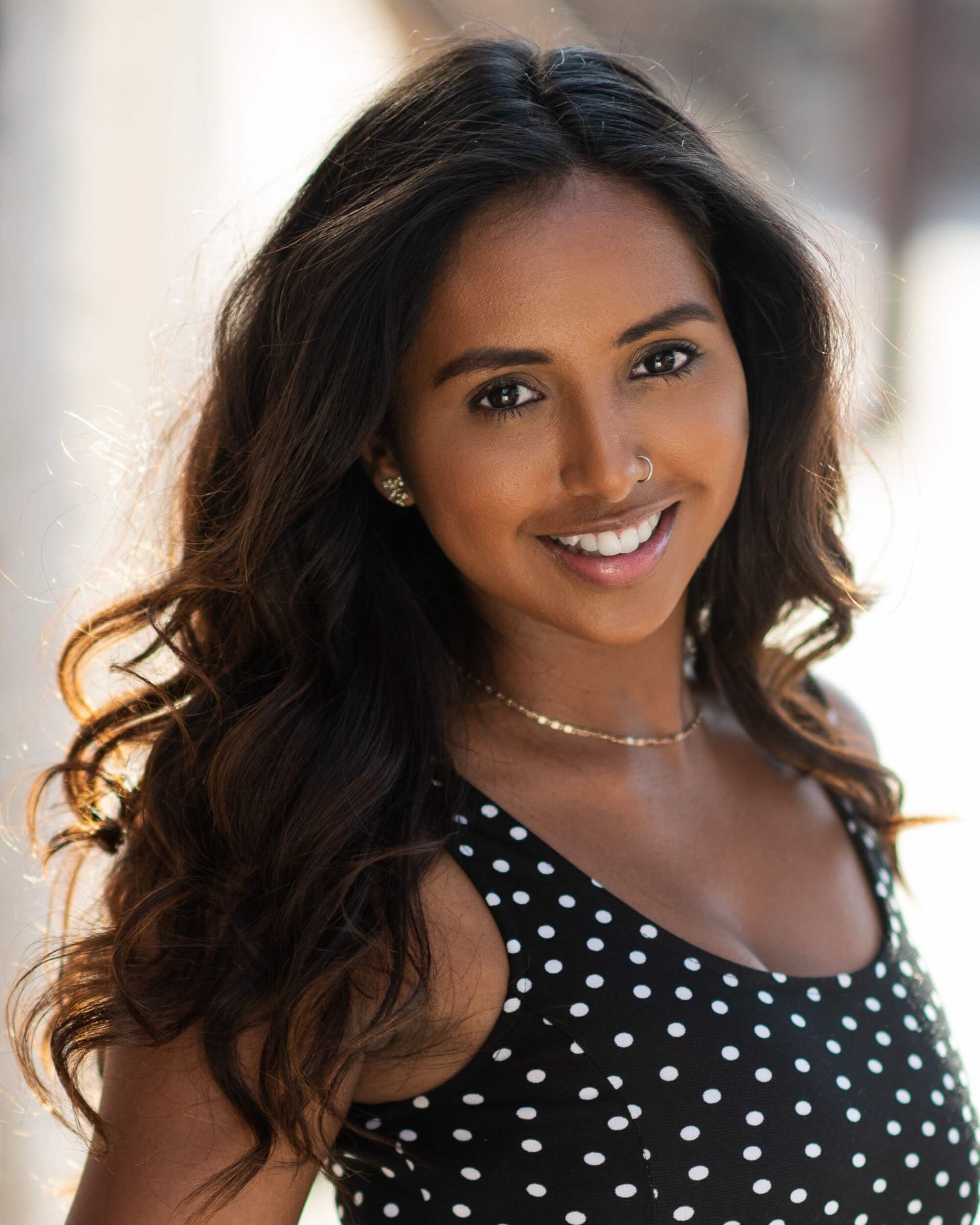 Smiling woman with long curly hair wearing a polka dot dress posing for an outdoor headshot.