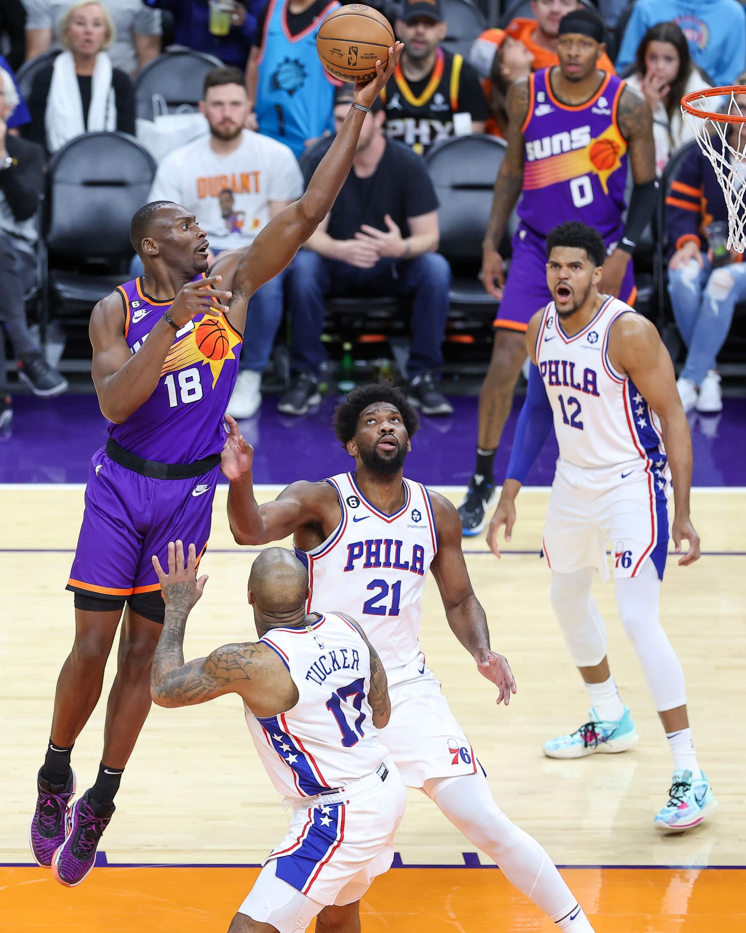 Phoenix Suns player number 18 drives to basket past Philadelphia 76ers defenders during NBA regular season game.