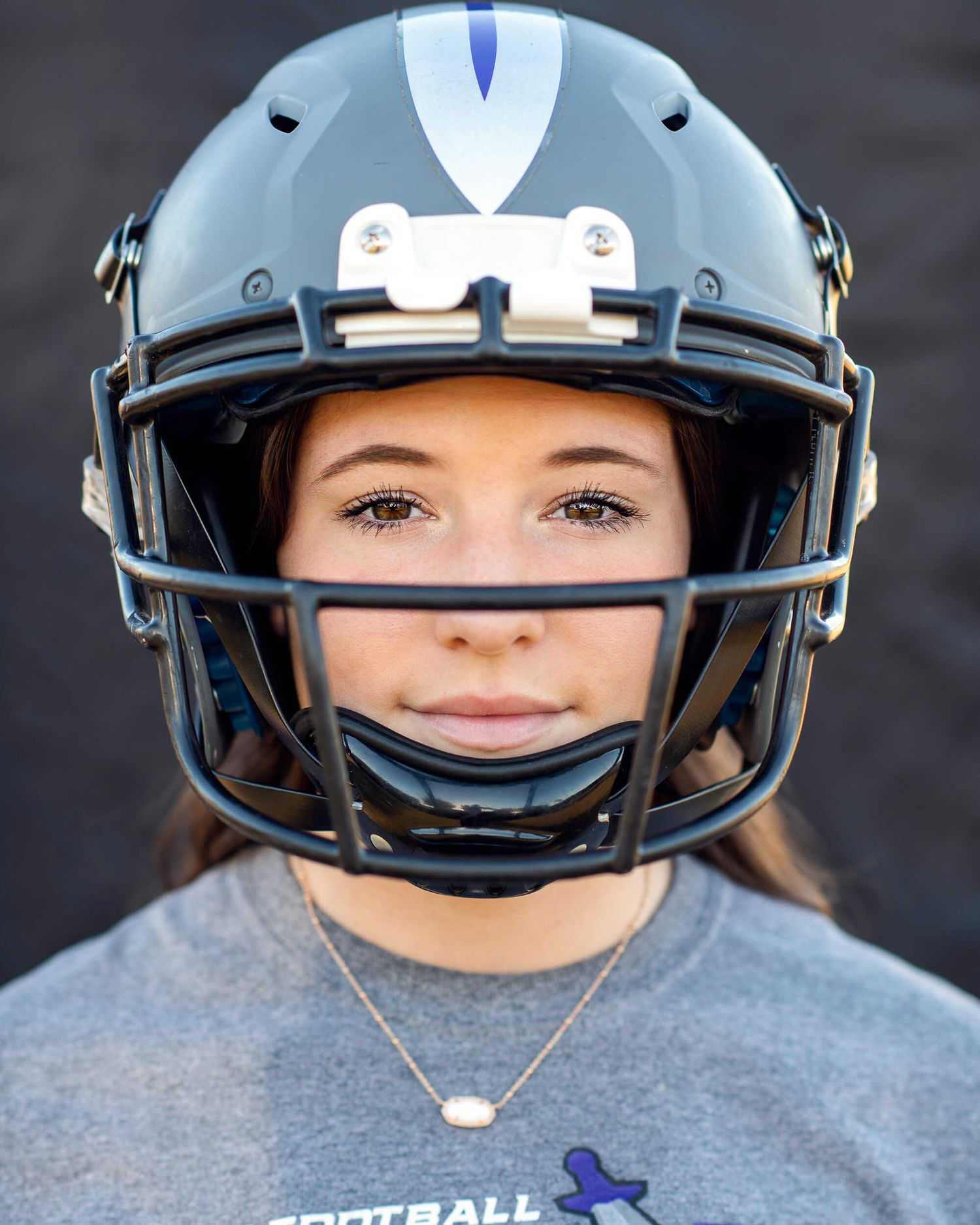 Young woman wearing a gray football helmet and jersey smiling for a sports portrait photo.