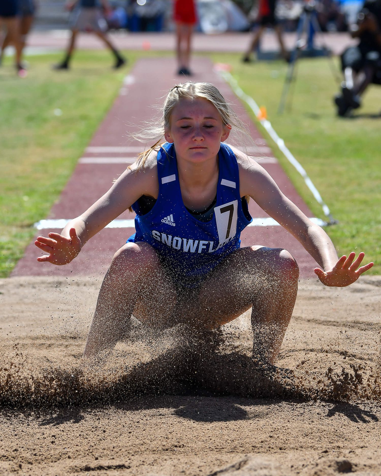 Snowflake athlete number 7 lands in sand pit during long jump at track and field meet.
