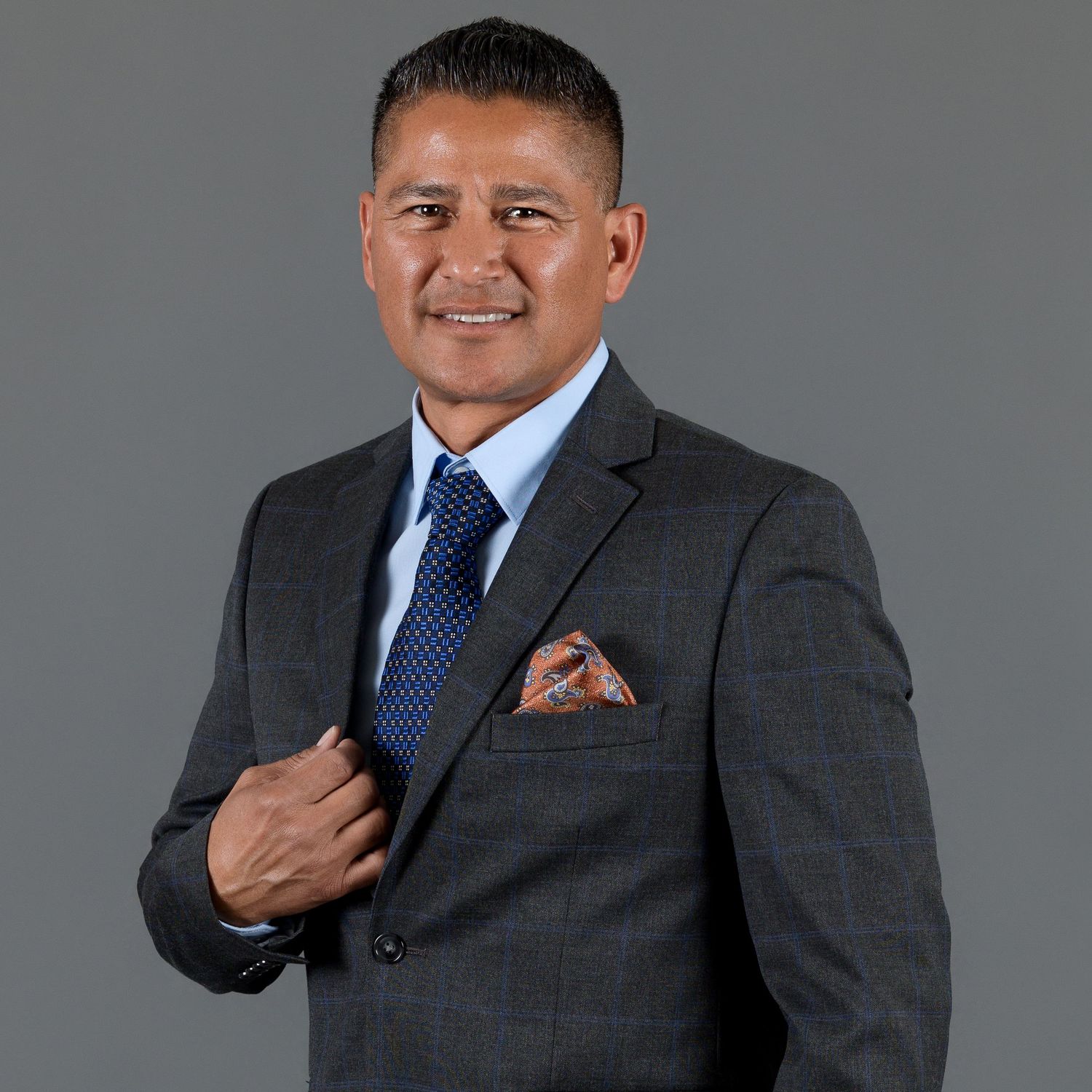 Professional man in gray suit and blue tie posing against gray background.
