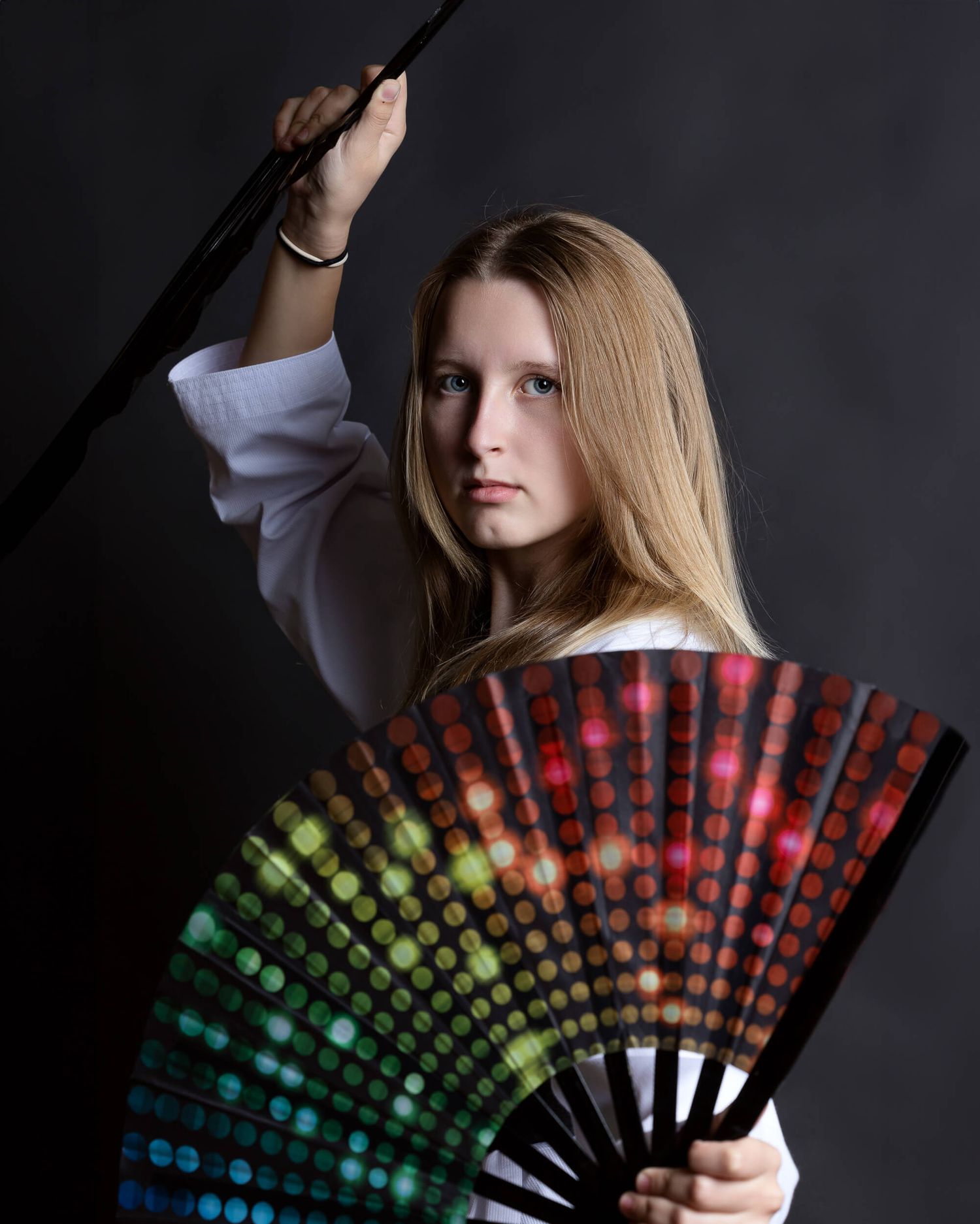 Young woman poses with colorful rainbow fan and black pole in studio.