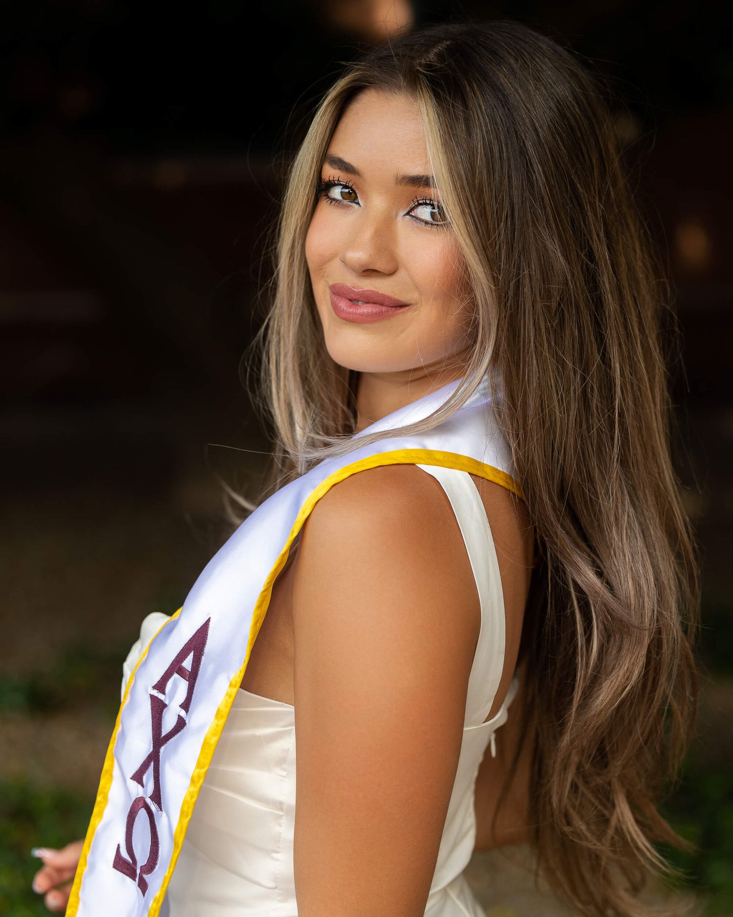 Close-up portrait of a graduate wearing an Alpha Chi Omega white and gold graduation sash.