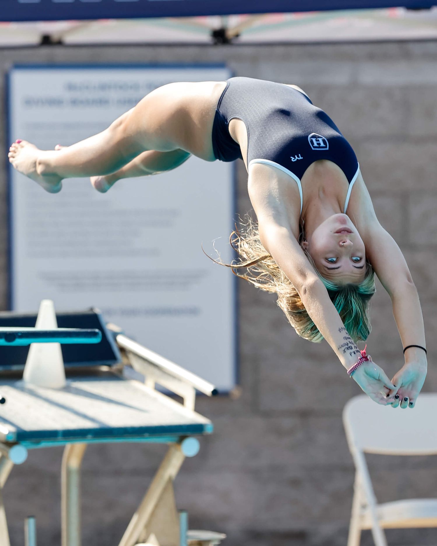Female diver performs a back flip off the diving board during a competitive diving meet.