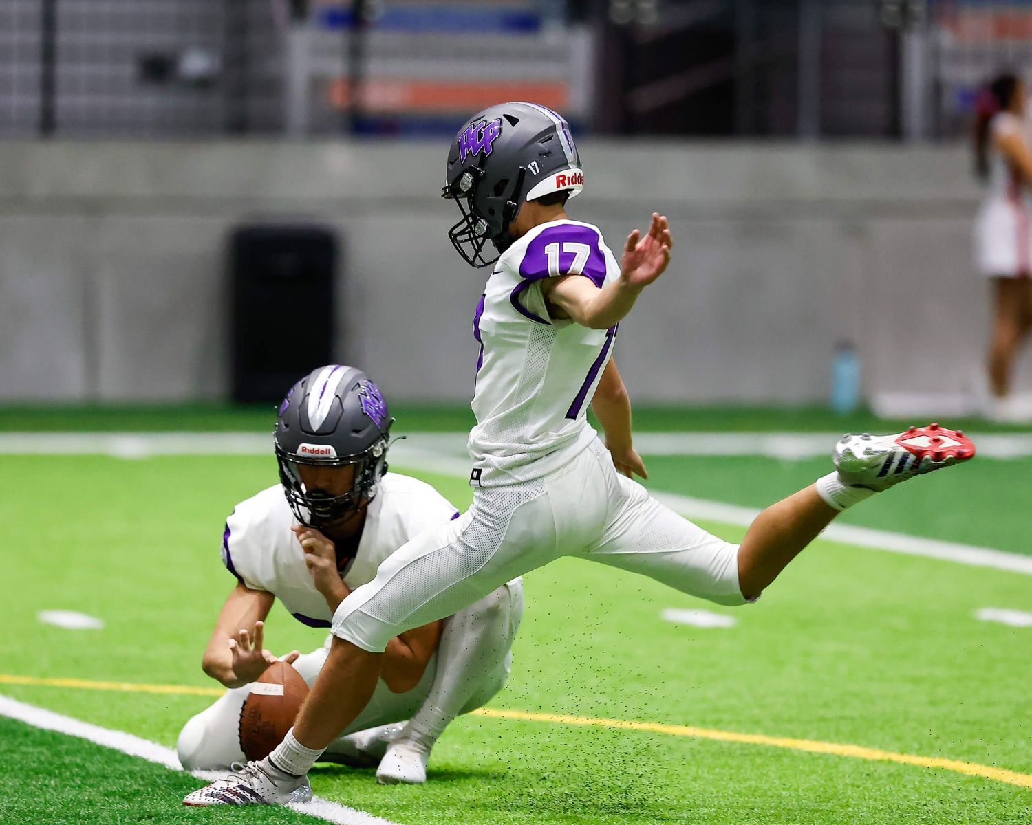 Football player #17 in purple uniform executes a field goal kick during indoor game.