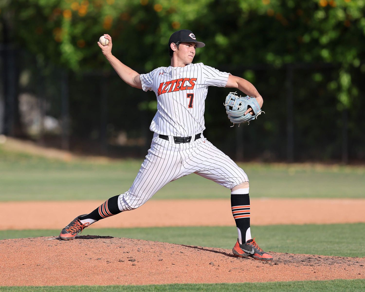 High school baseball pitcher in pinstripe uniform winds up to deliver a pitch.