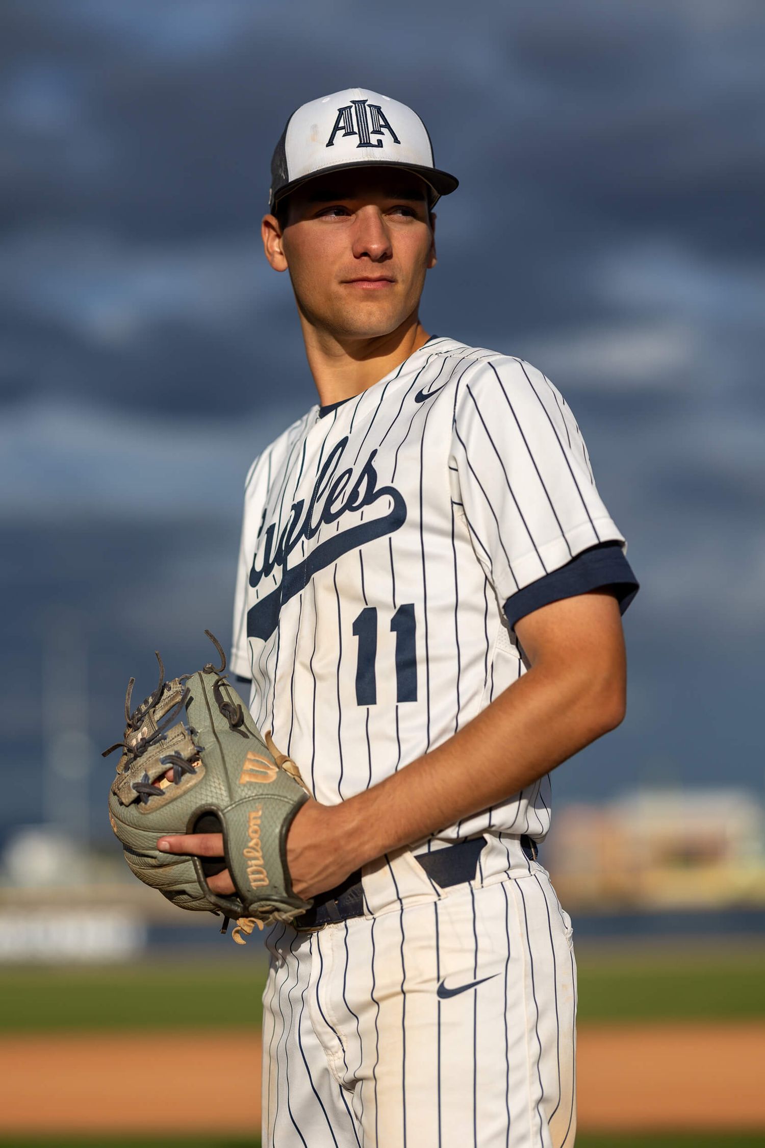 Young male baseball player in Eagles uniform number 11 holding a glove on a field.