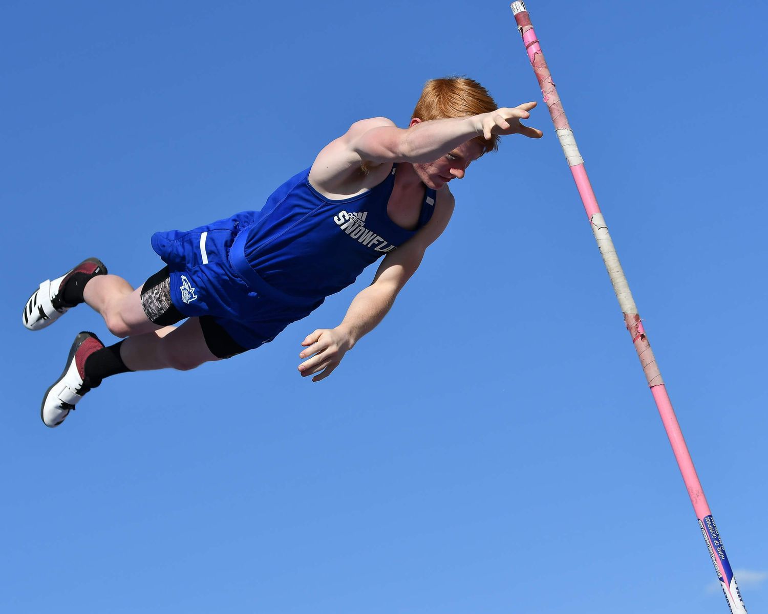 Male pole vaulter clears the bar in a dynamic blue sky outdoor track competition photo.