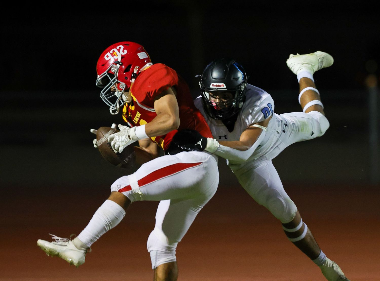 Two football players compete for the ball during an intense night game under stadium lights.