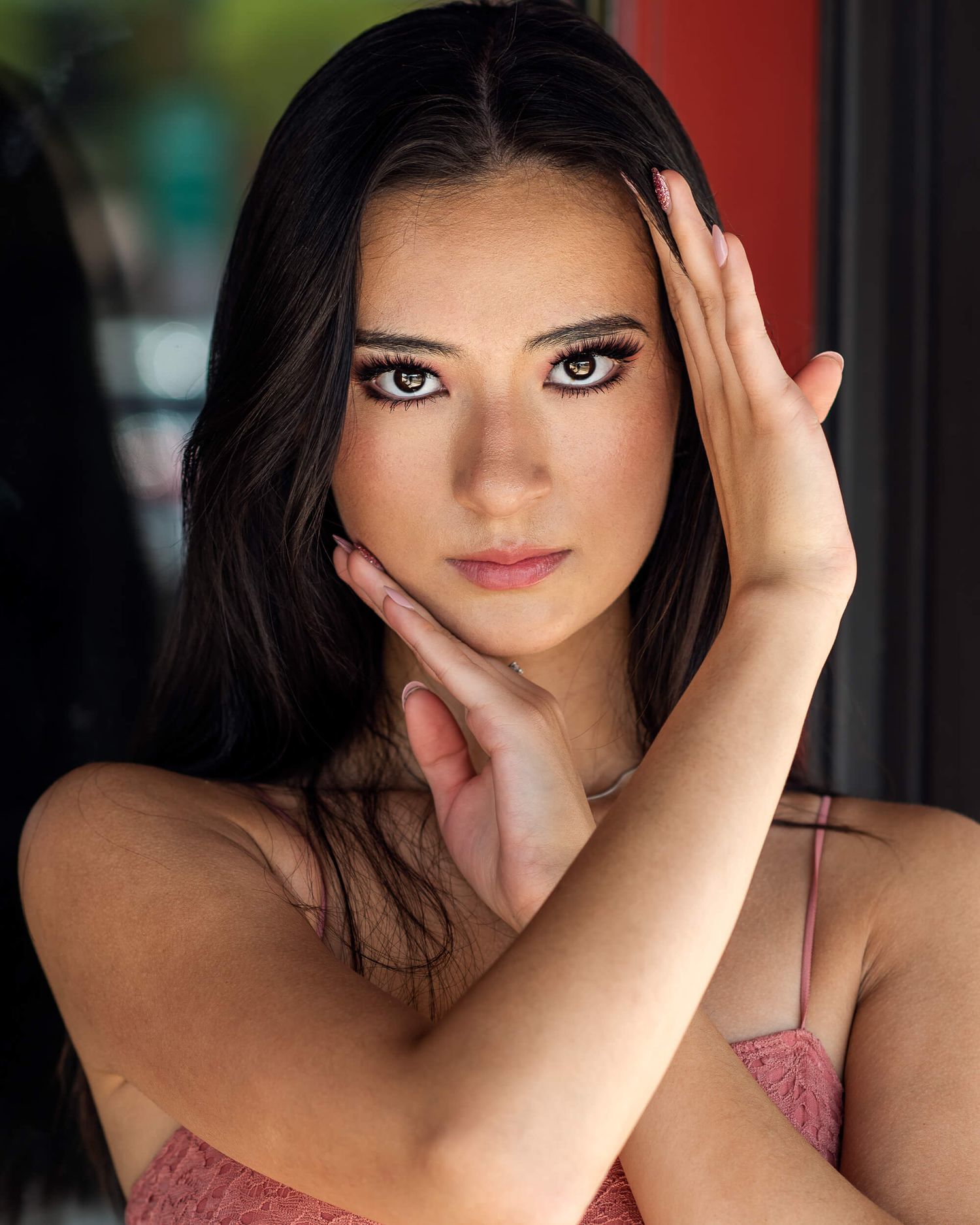 Dark-haired woman with hazel eyes and glam makeup posing in a pink top for a modeling headshot.