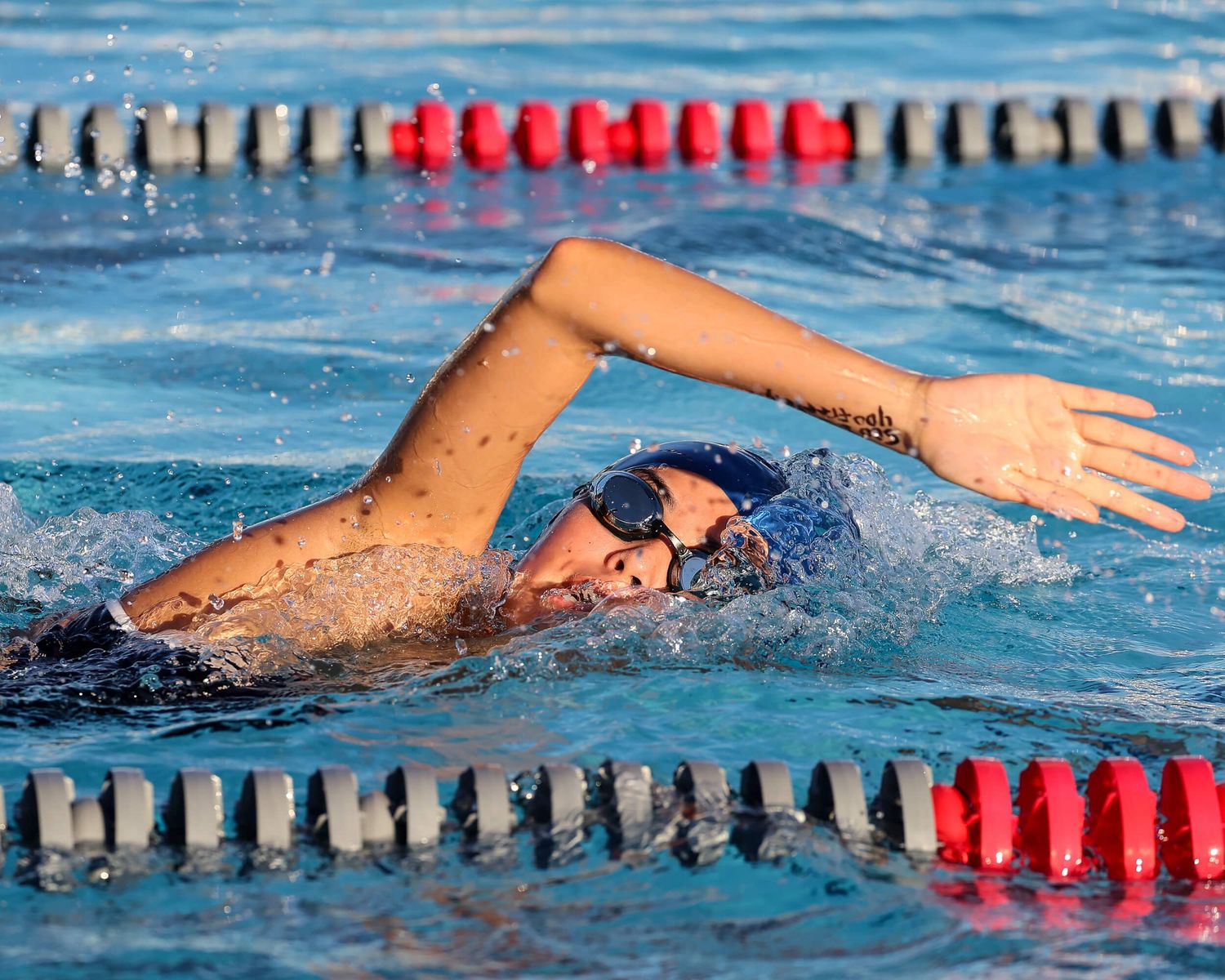 Competitive swimmer performs freestyle stroke in outdoor pool during race.