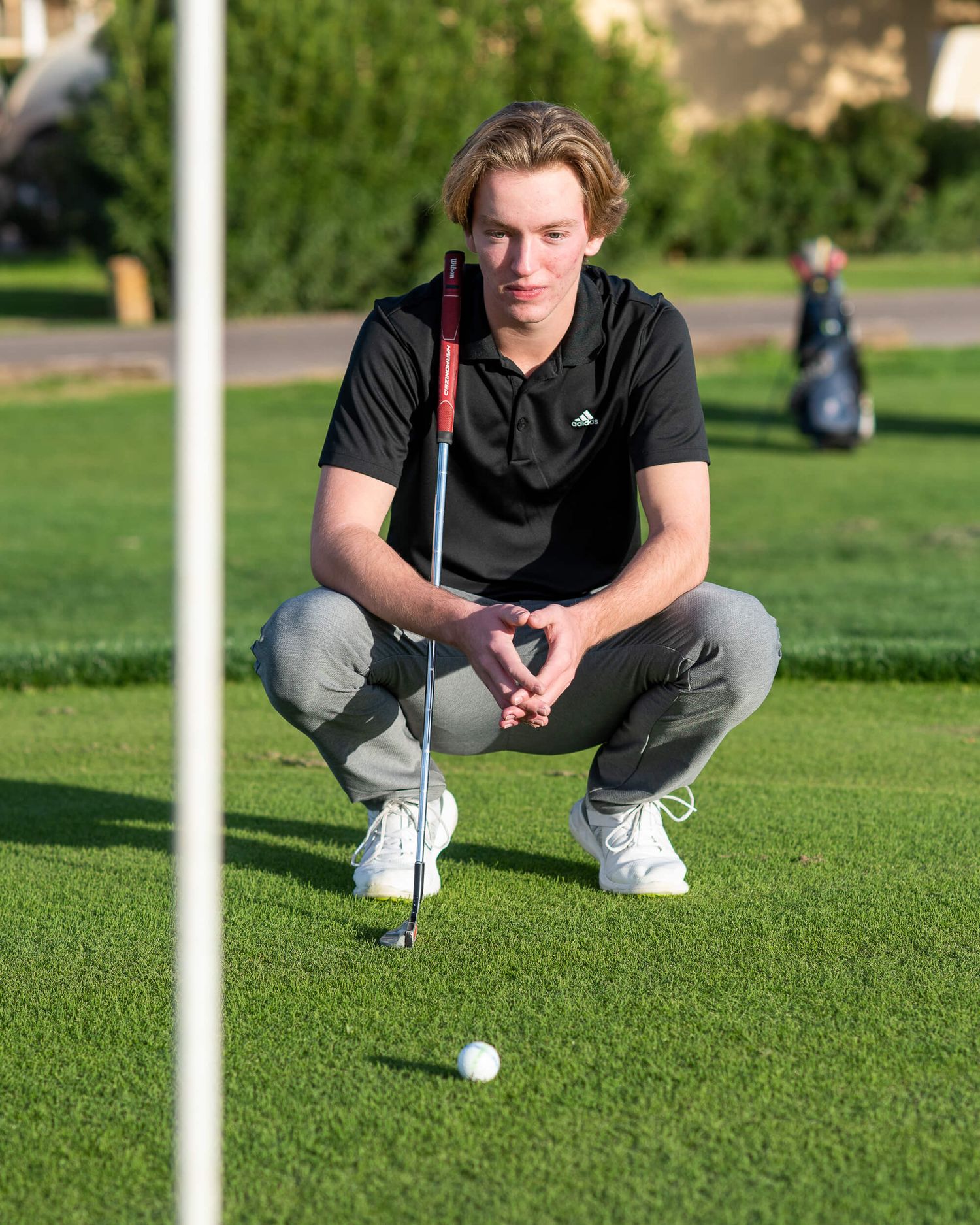 Young male golfer crouches to read green before putting during golf match.