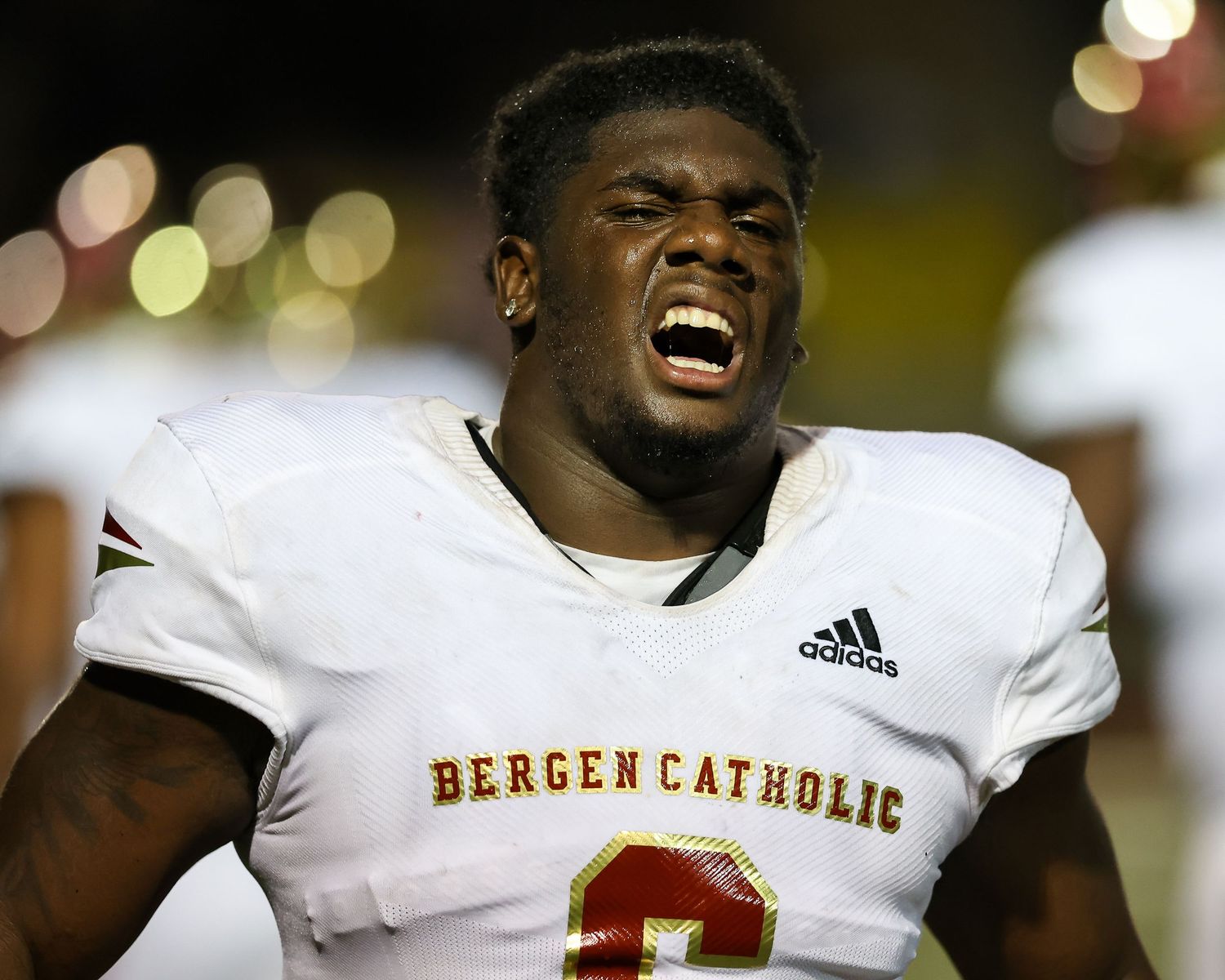 Football player in Bergen Catholic white jersey celebrating on field at night game.