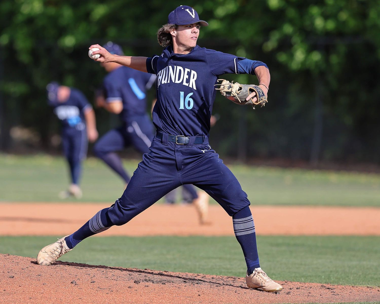 Baseball pitcher #16 in navy Thunder uniform winds up to throw during an outdoor game on a sunny day.