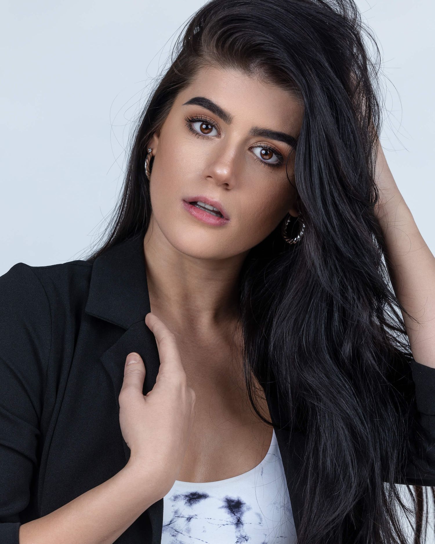 Young woman with long black hair in a black blazer posing against a white background for a headshot.
